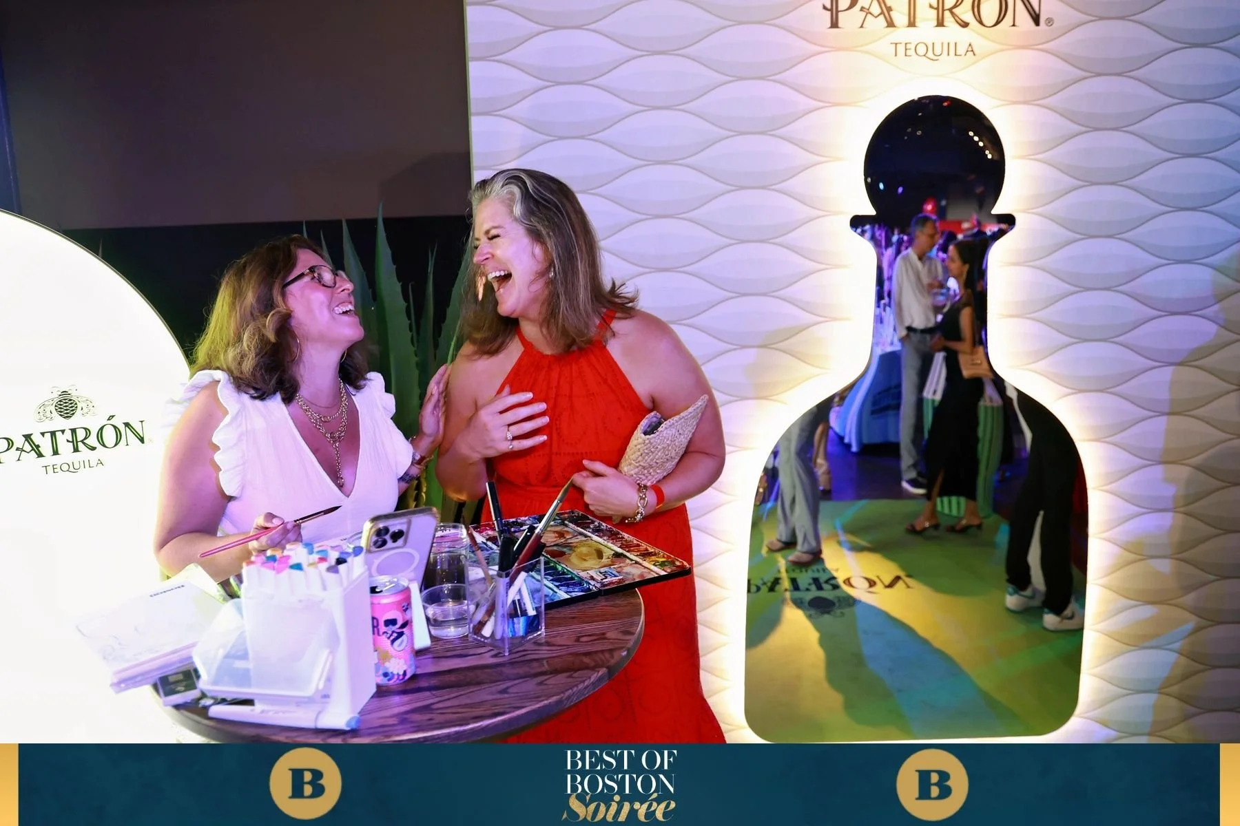 Corporate event guest wearing a halter dress laughs with the live artist as she paints as event entertainment.