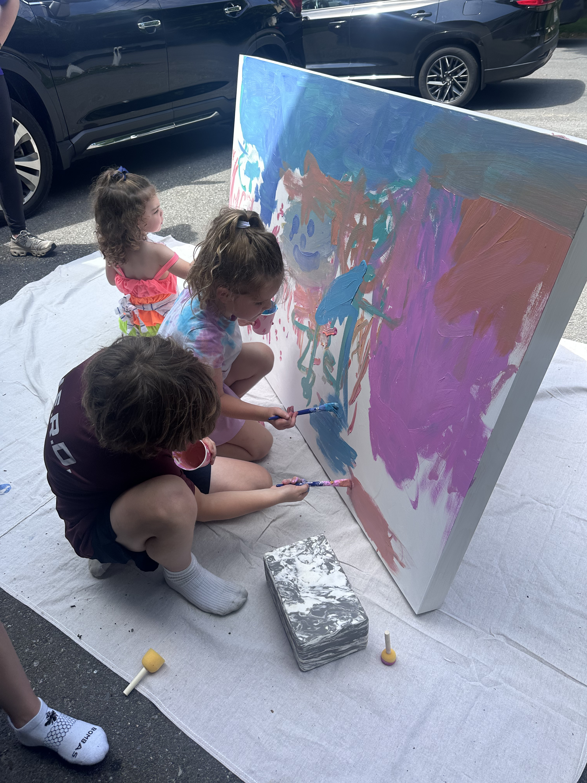 A group of children paint on a large canvas together