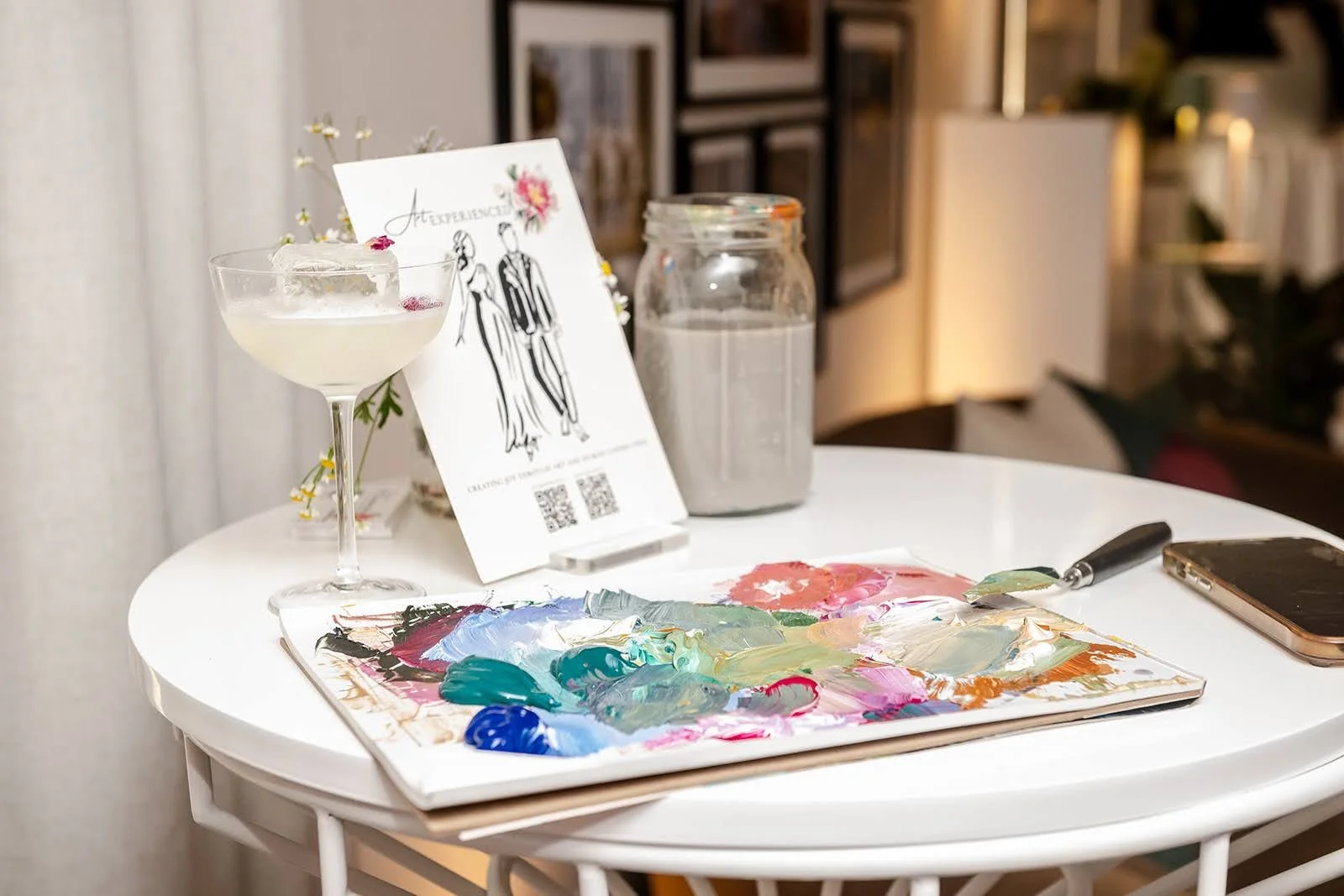 A paint palette sitting on a small table next to a glass of wine and a sign