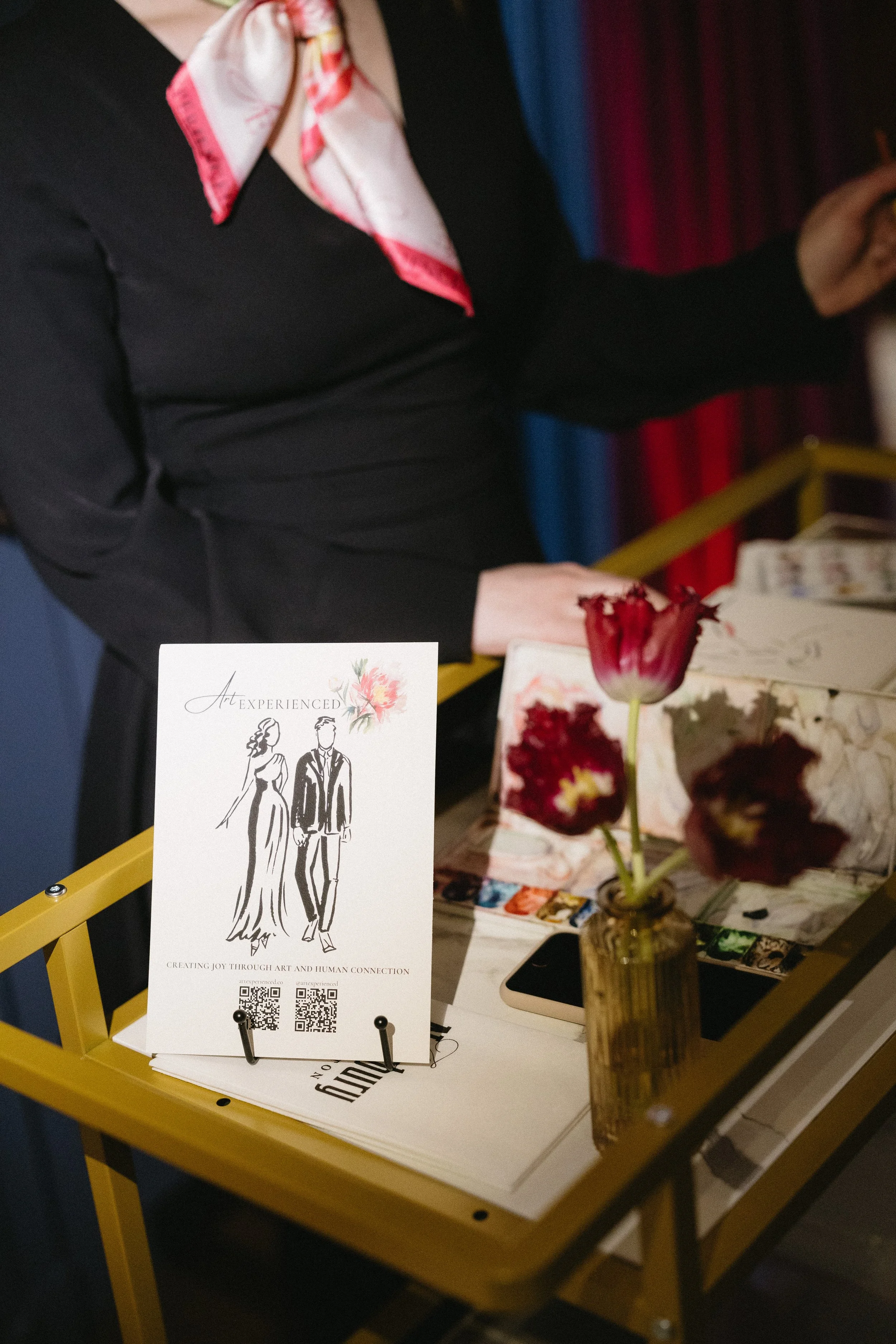 a styled "art experienced" sign sits on a cart as an artist paints next to it