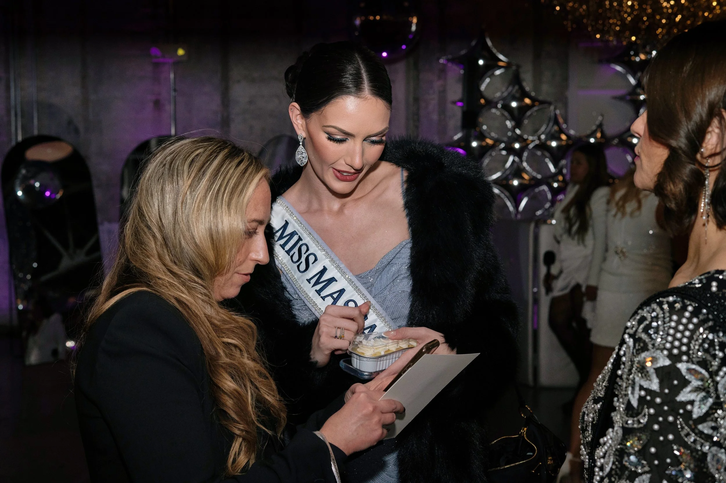 Miss Massachusetts smiles and looks at a painting with a guest