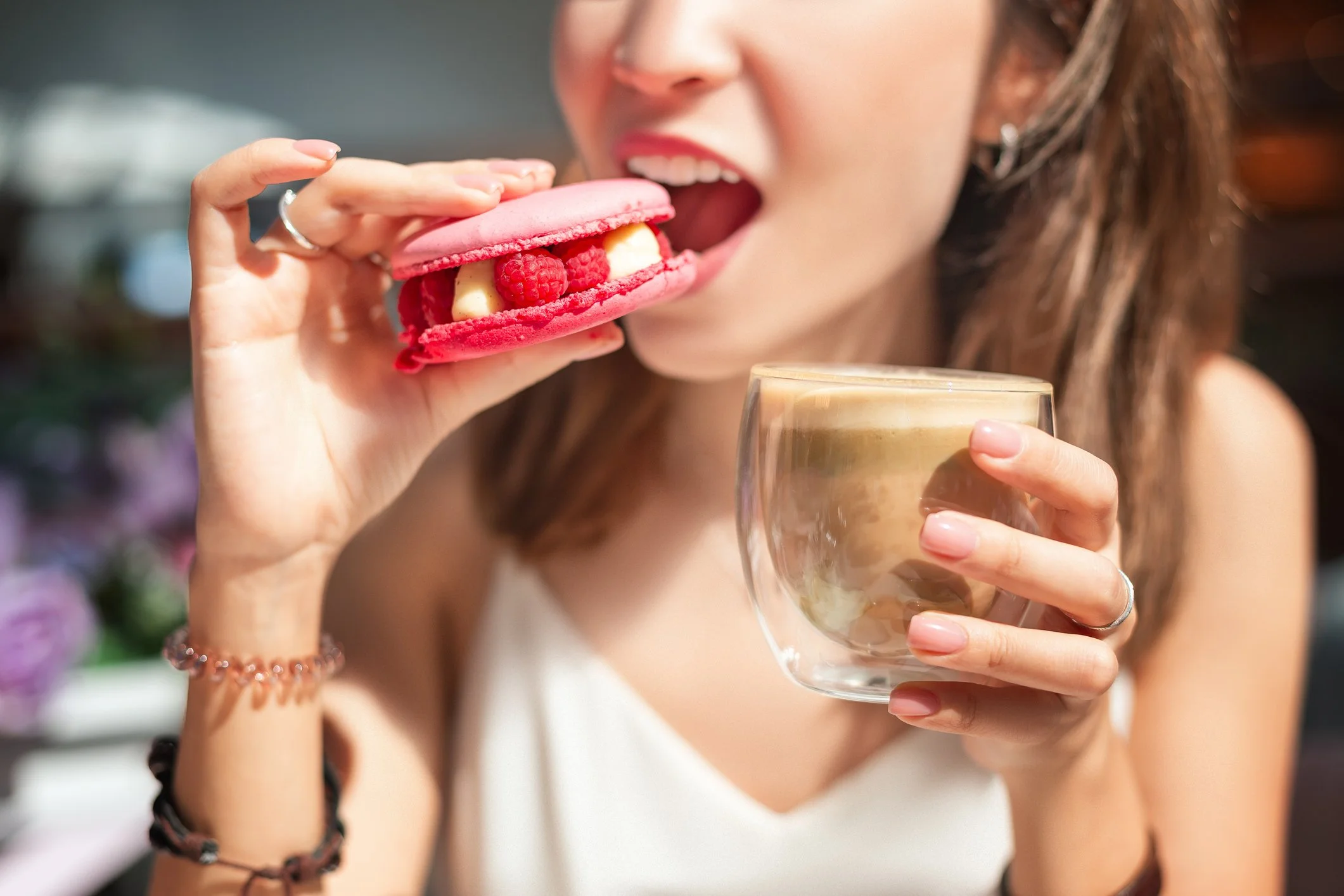woman eating a pink dessert and holding a cup of coffee 