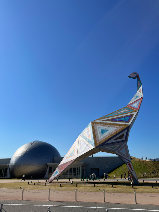 The Fukui Dinosaur Museum looks like an egg. An art installation of a dinosaur stands over it.