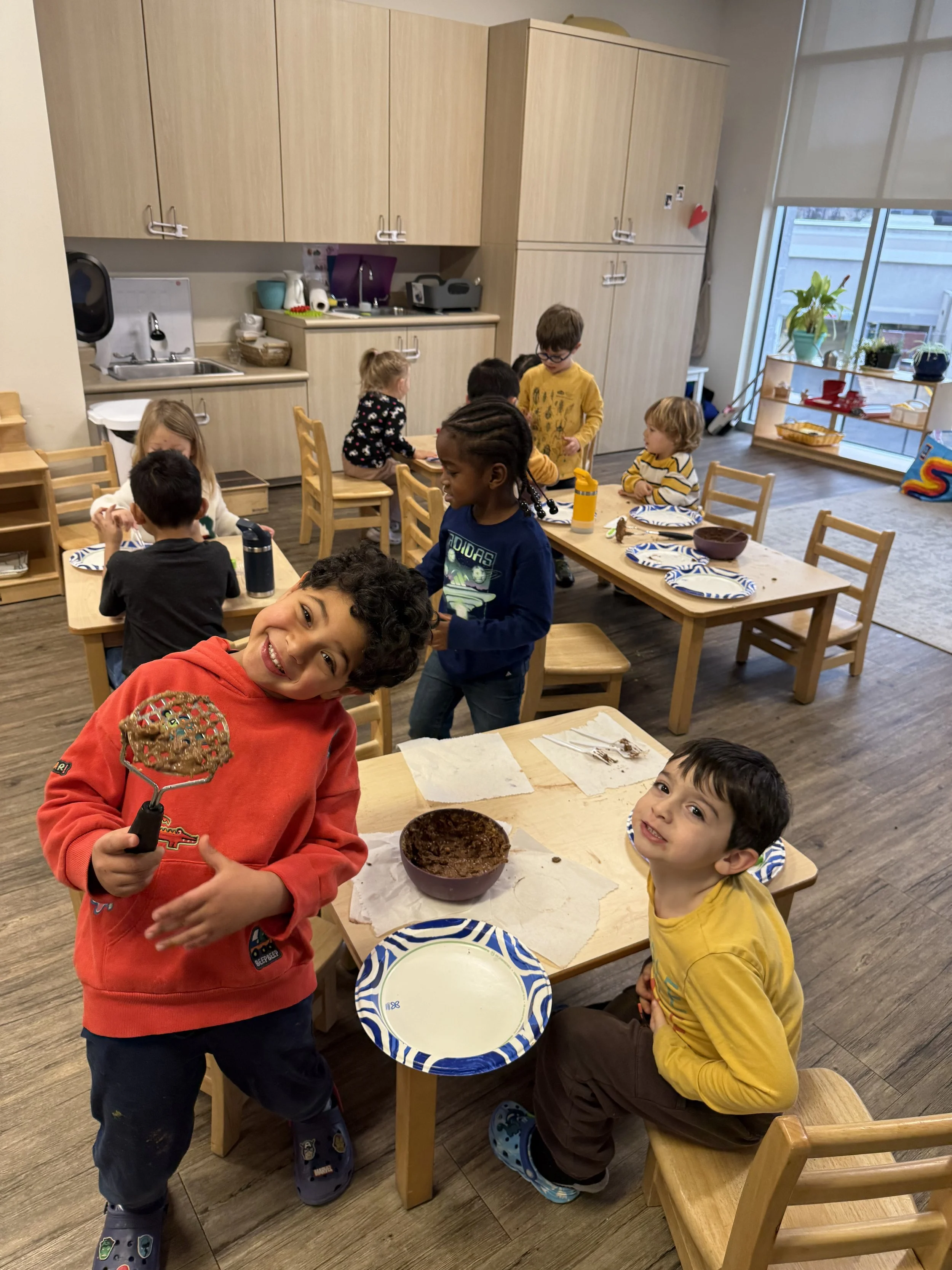 Children in aprons smiling and cooking together in a classroom setting.
