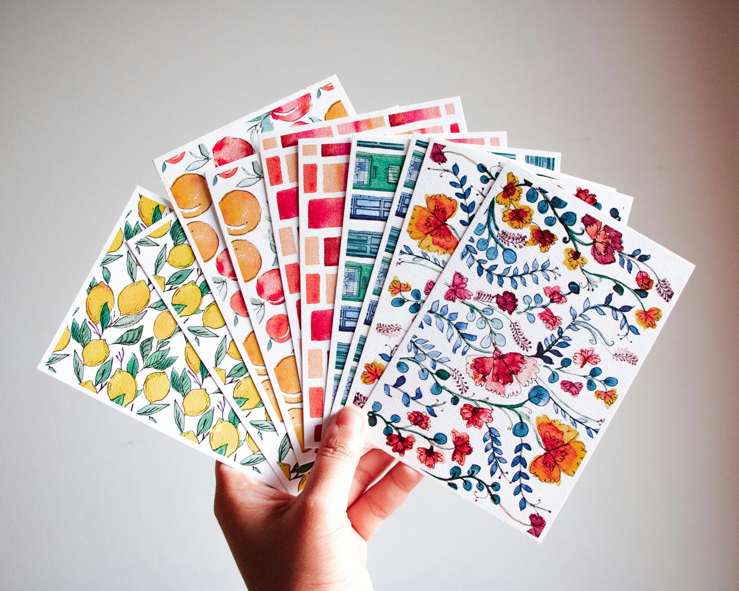 Hand holding a fan of colorful floral and geometric patterned papers or cards.