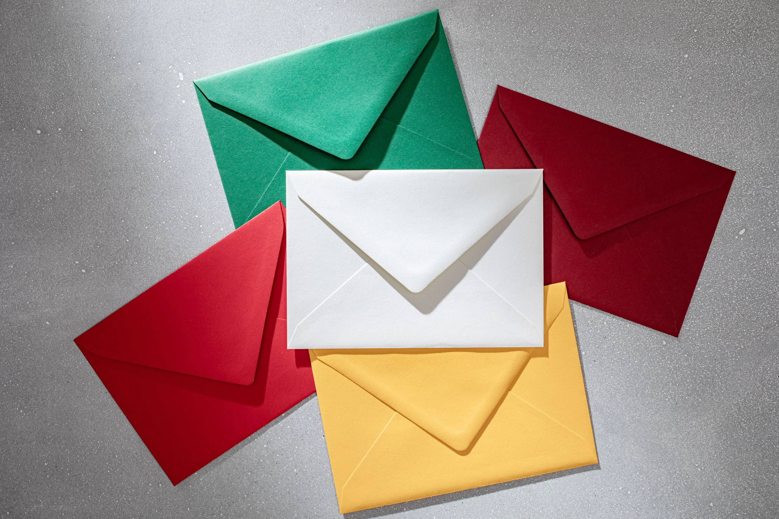 Six colorful envelopes in green, red, white, and yellow, arranged on a gray, textured surface.