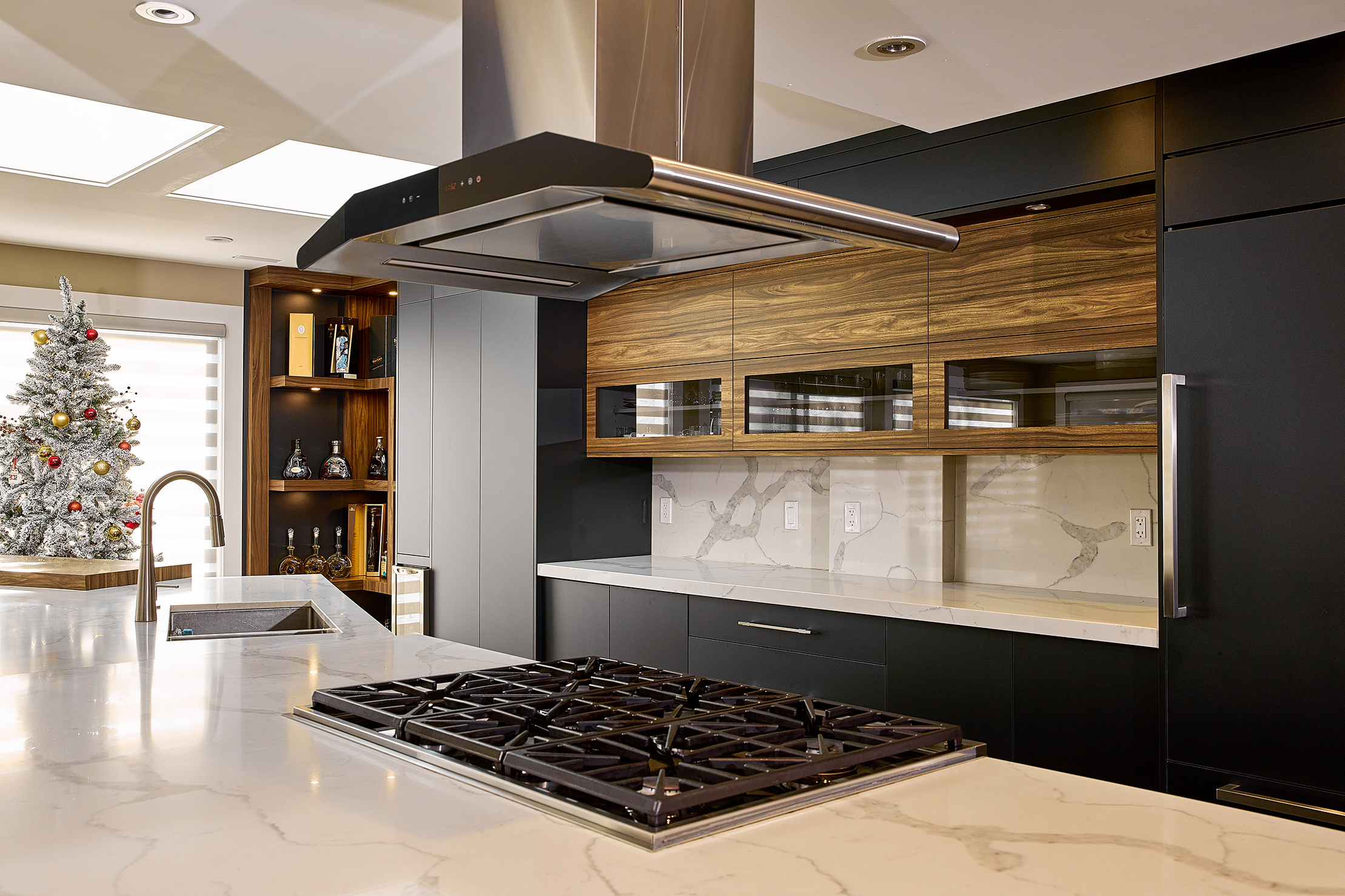 Modern kitchen with stovetop, marble countertops, wood cabinets, gray cabinets, and a Christmas tree.