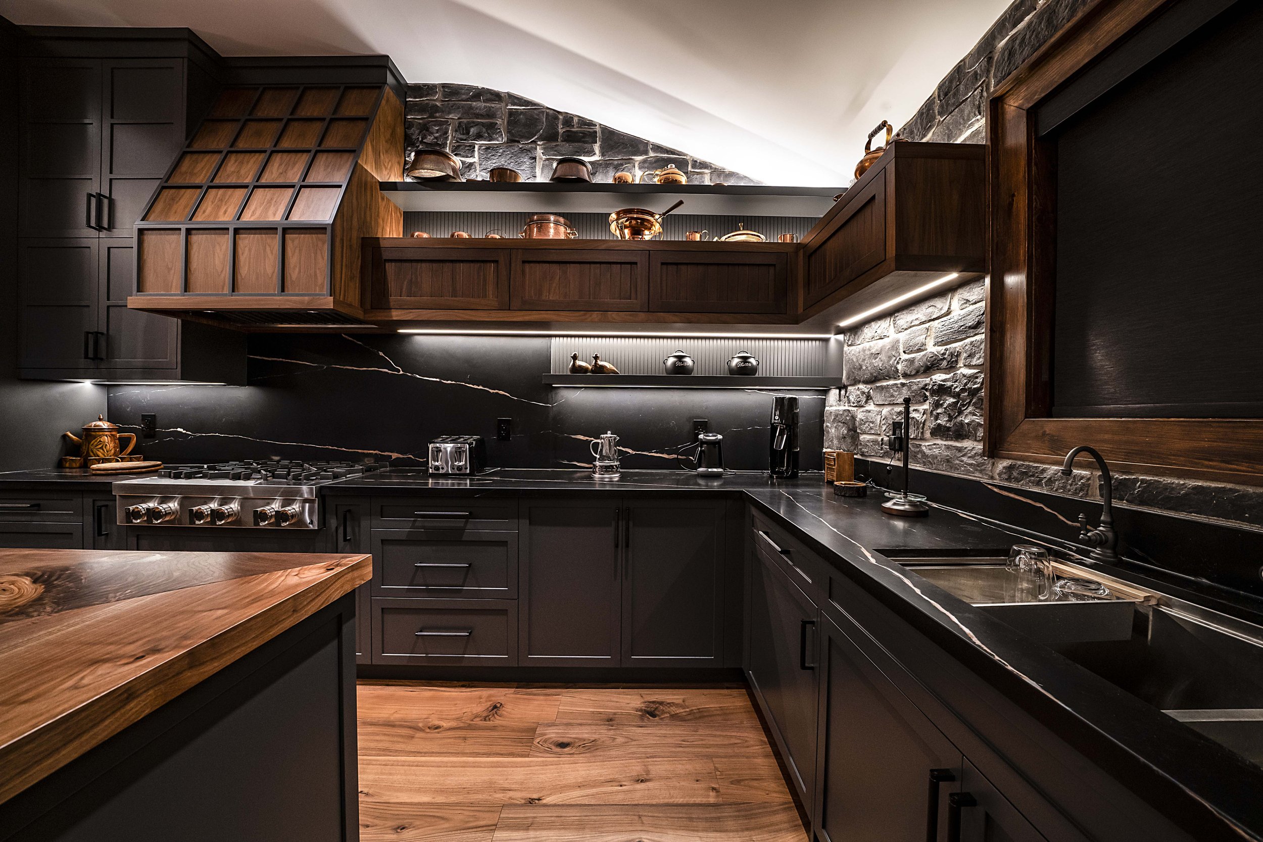 Modern kitchen with dark cabinets, wooden accents, and stone wall