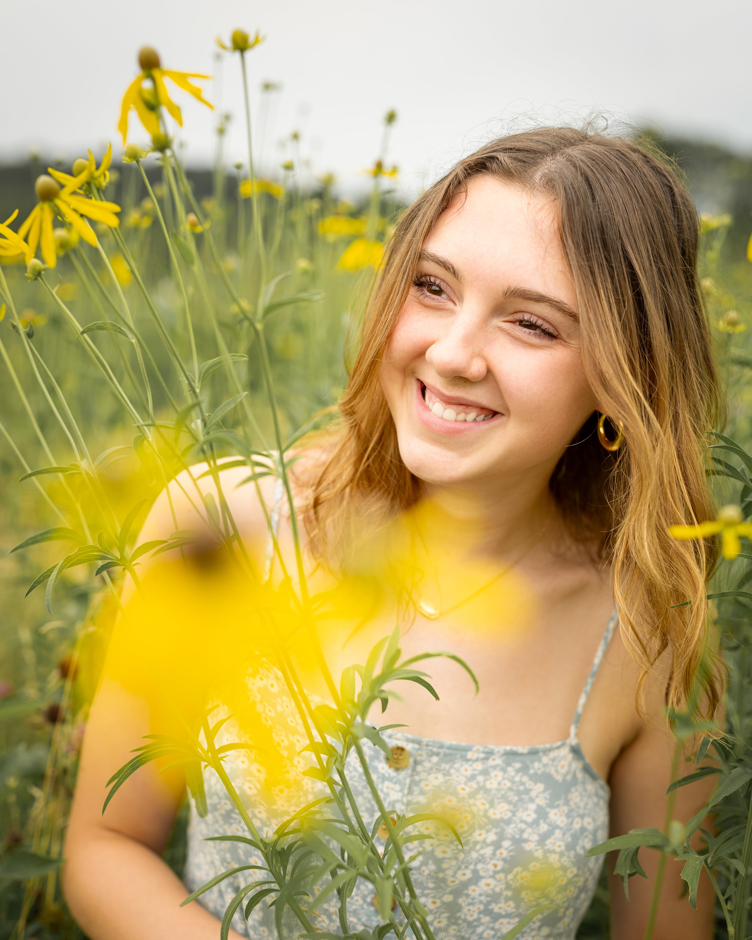 Young woman smiling in a field of yellow wildflowers for her outdoor themed senior pictures in Merrimac, WI.