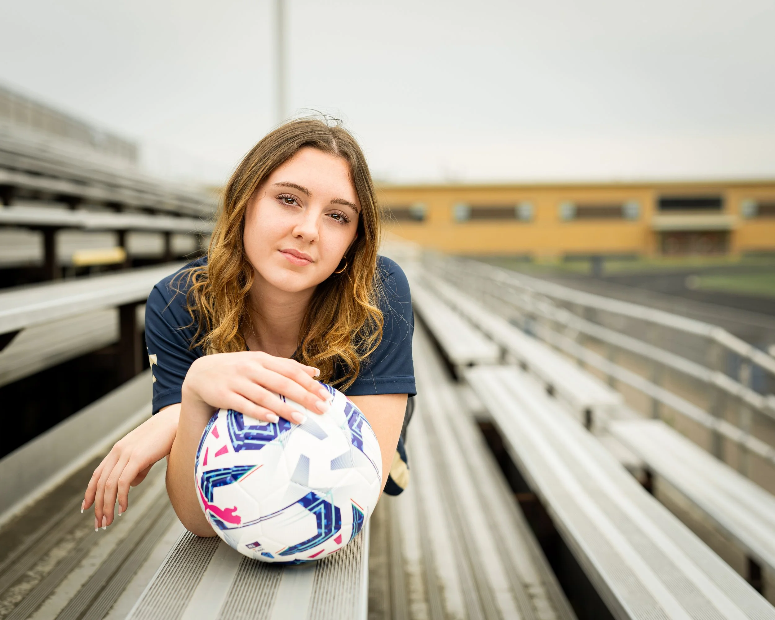 Young woman with soccer ball sitting on bleachers