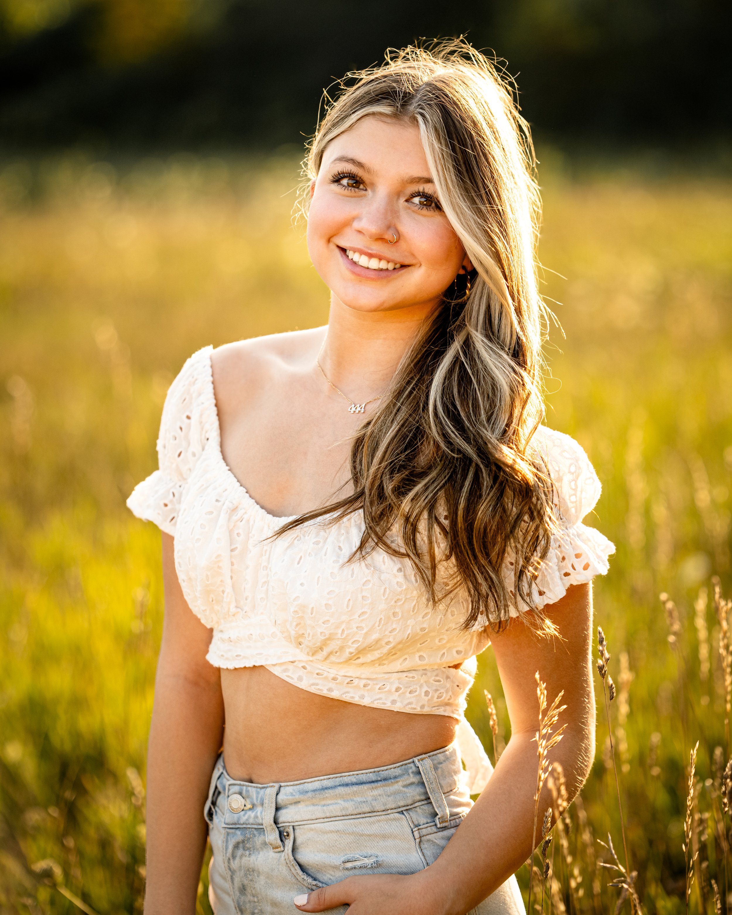 Woman in a white lace top and denim shorts smiling in a sunny field.