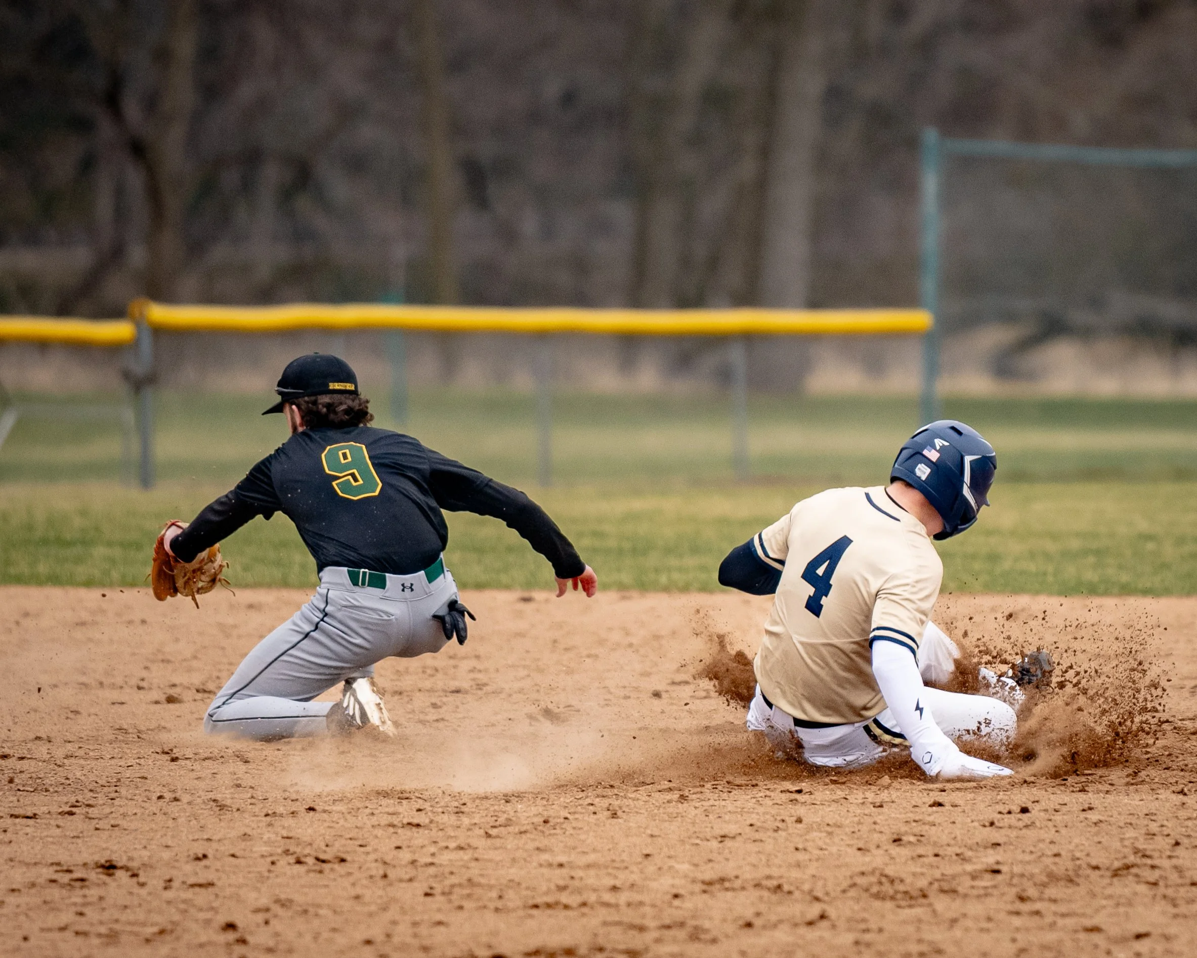 Baseball game action with a player sliding into a base while another player attempts to tag them out.