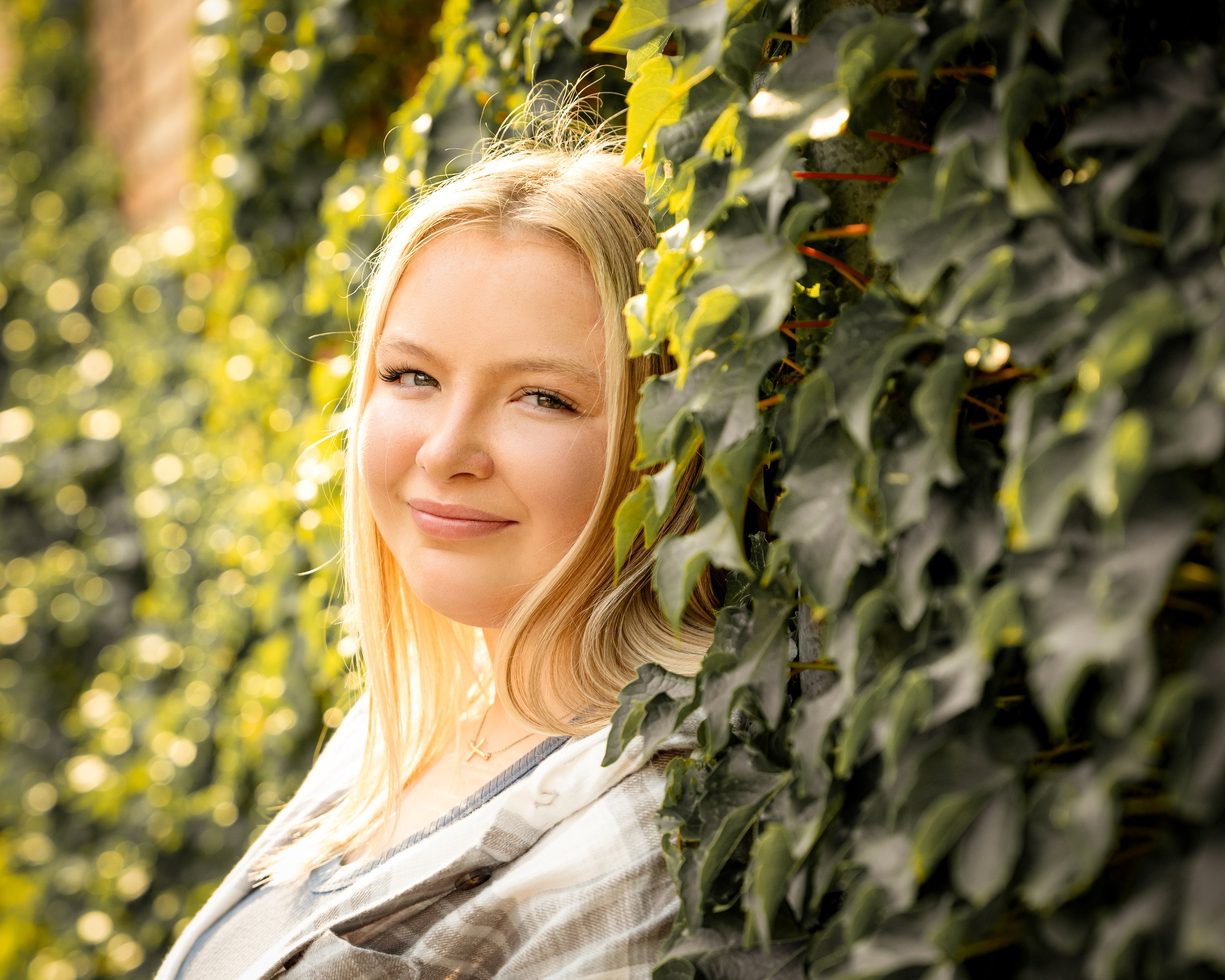 Smiling person leaning against a wall covered in green ivy.