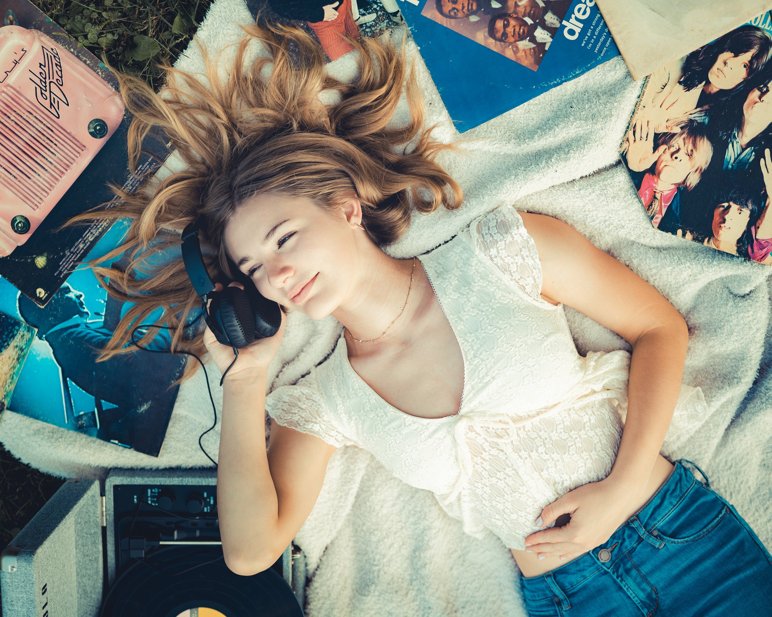 Young woman lying on a blanket outdoors, listening to vinyl records on headphones for her vintage inspired senior portraits near Baraboo, WI