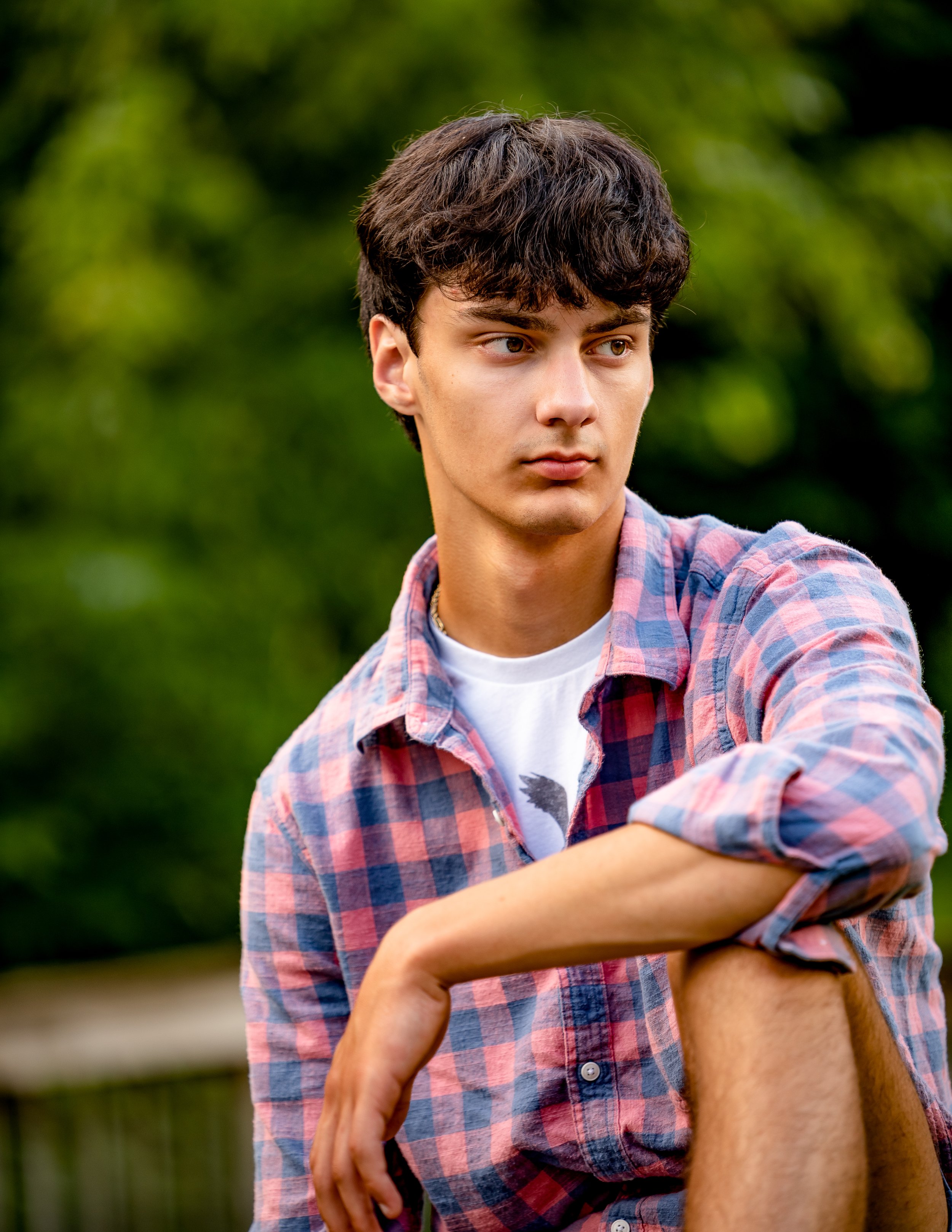 Young man in a checkered shirt sitting outdoors.