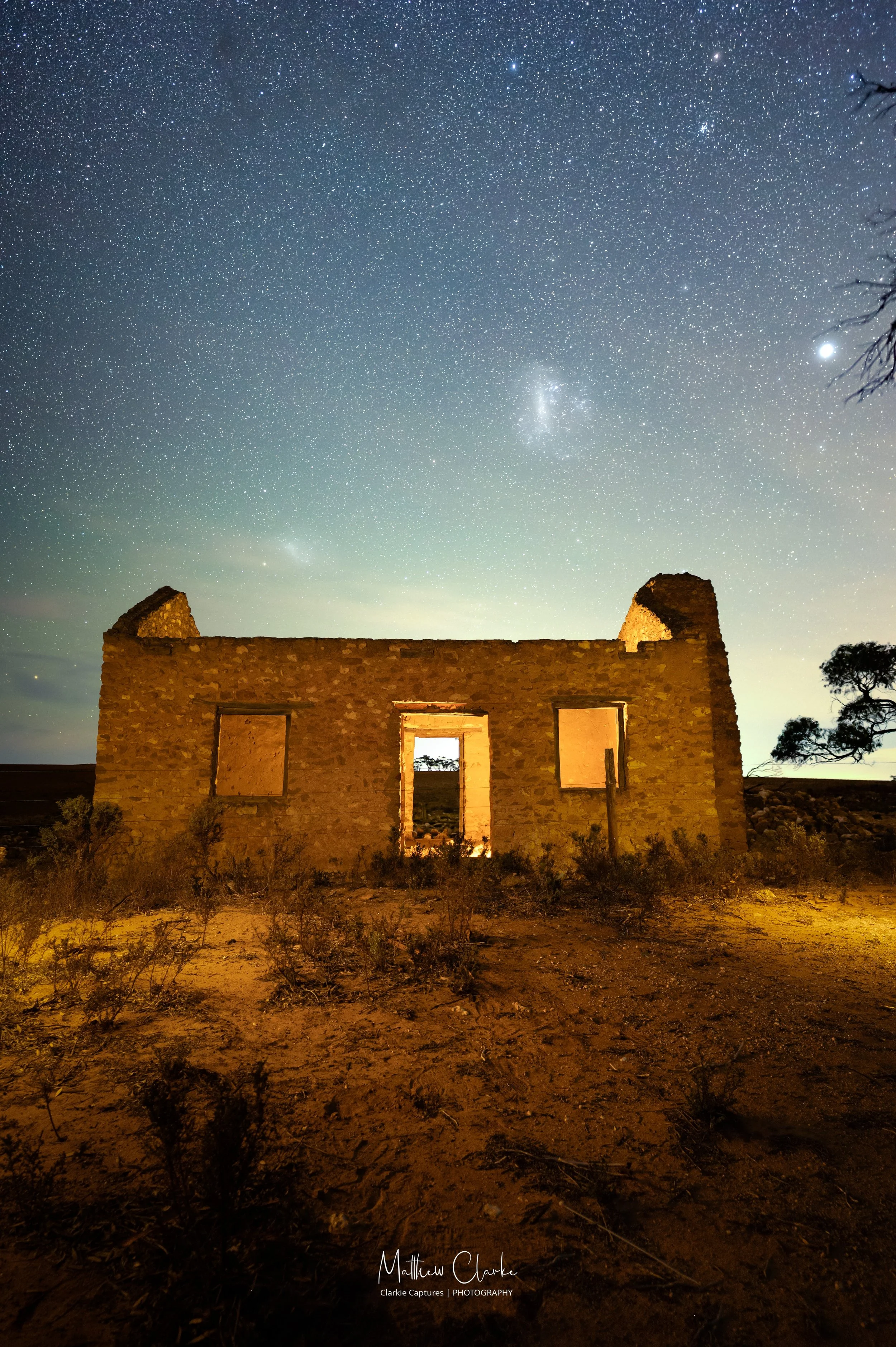 Ruined stone building in desert under a starry night sky with visible clouds and a bright star or planet.