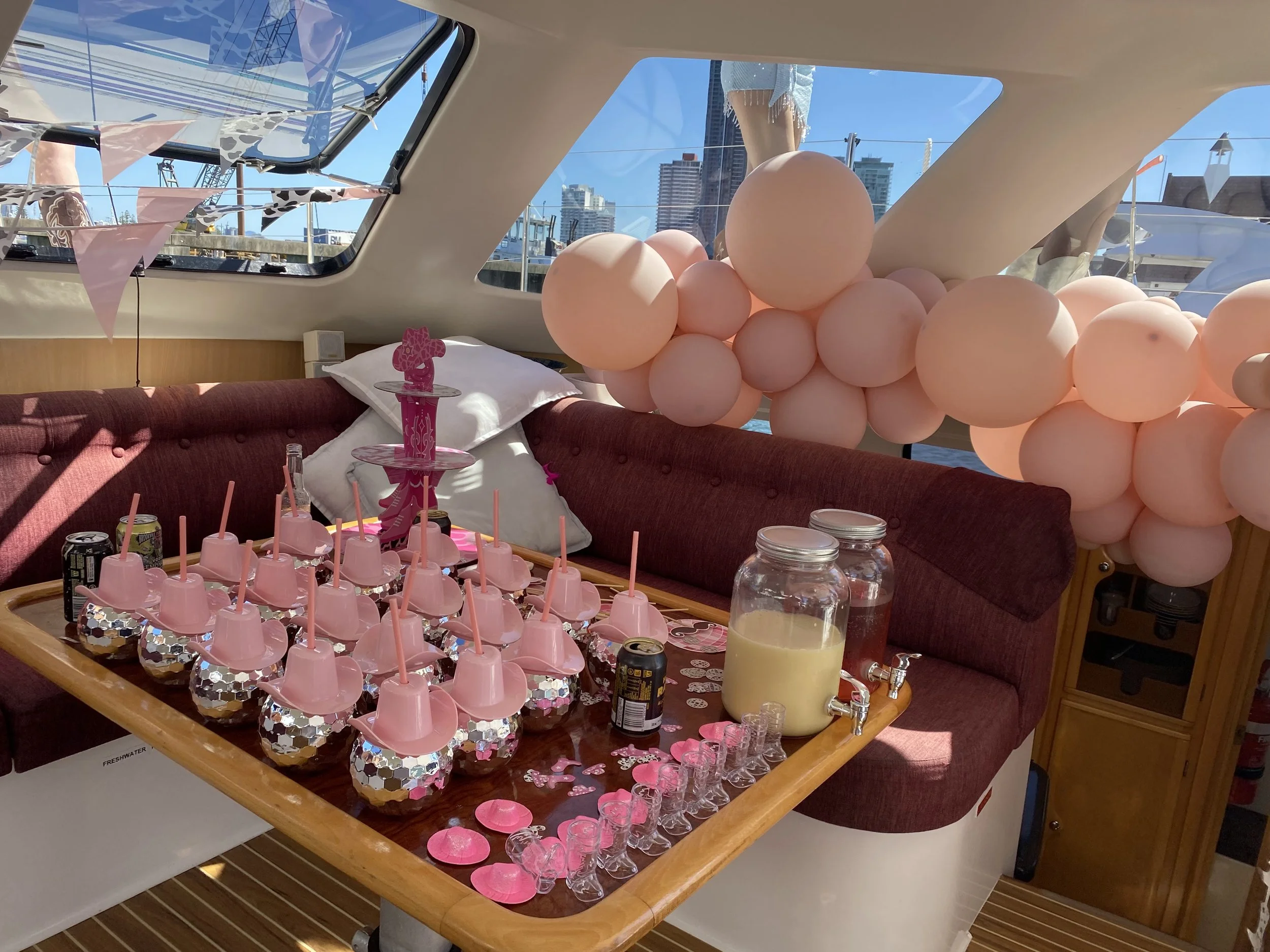 Inside a boat decorated for a birthday party with pink balloons, pink and silver party hats on cupcakes, drinks, and decorations.