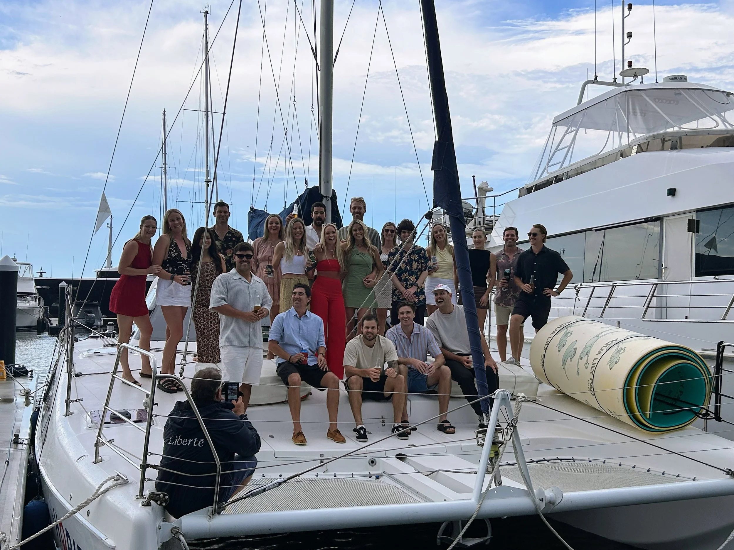 Group of people on a yacht docked at a marina, celebrating with drinks on a partly cloudy day.