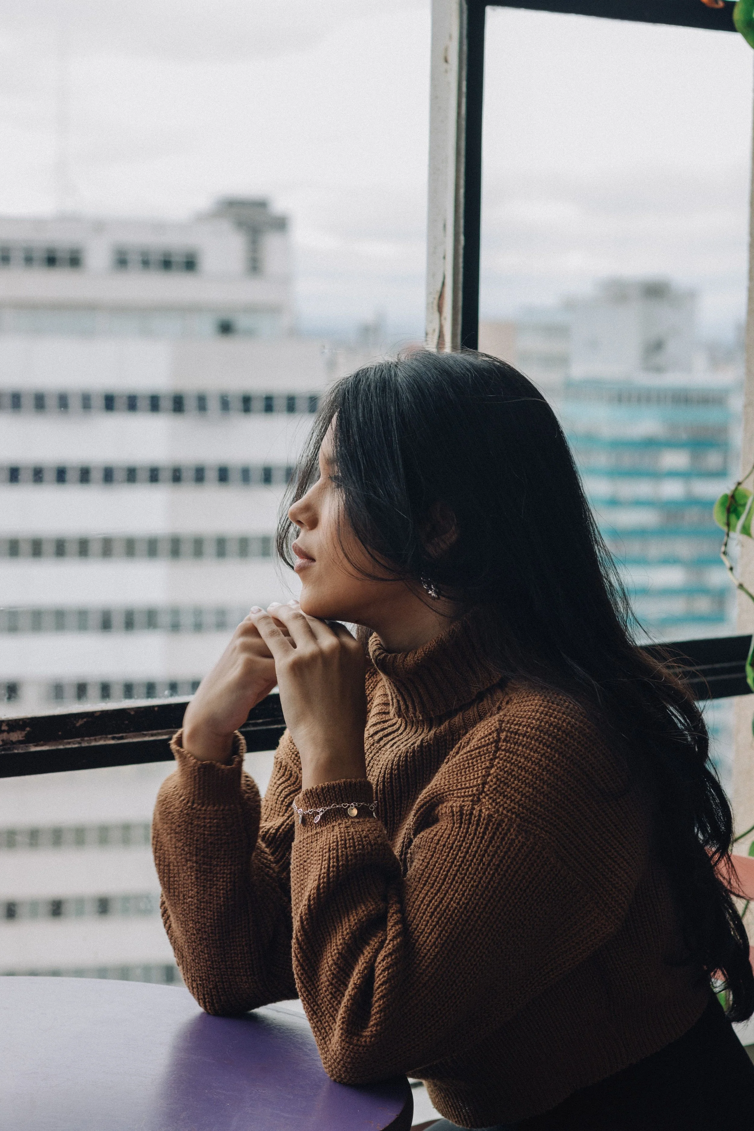 A woman resting her chin on her hands, looking thoughtfully out a window
