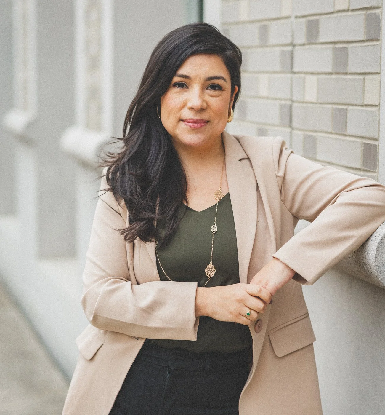 Karol Espejo, LCSW, a bilingual therapist, smiling and leaning against a brick wall