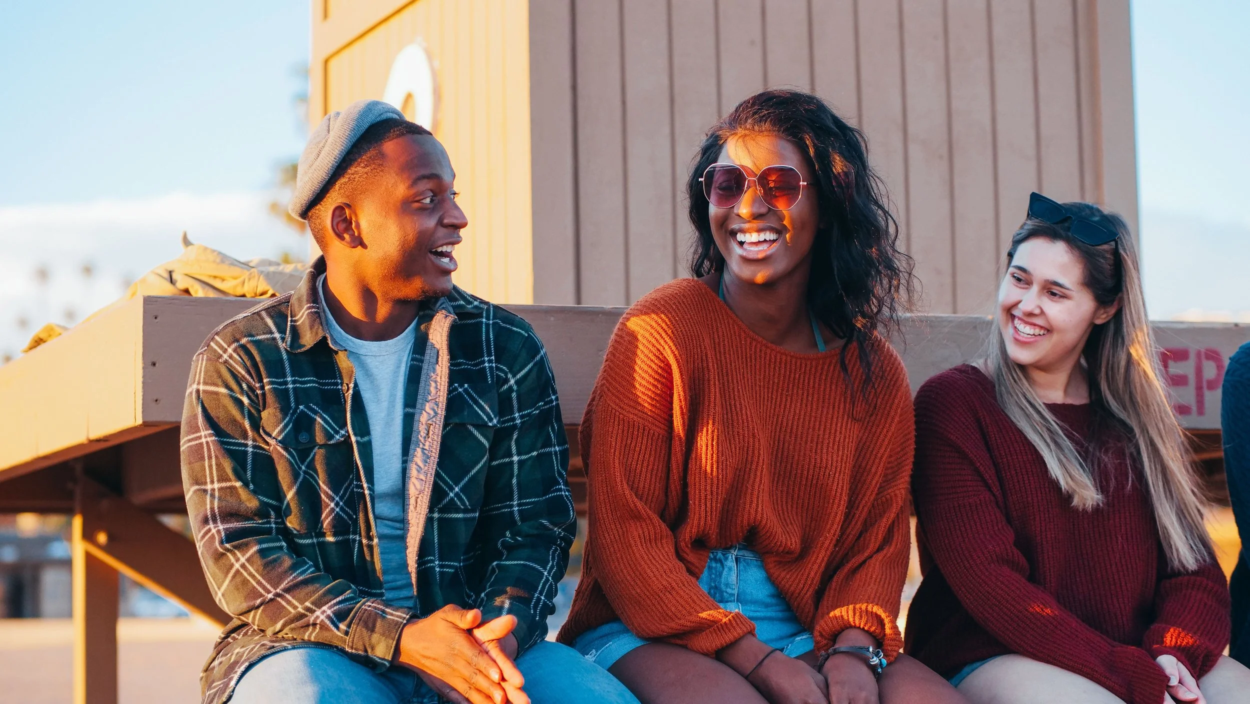 Three friends sitting together outside at sunset, laughing and talking