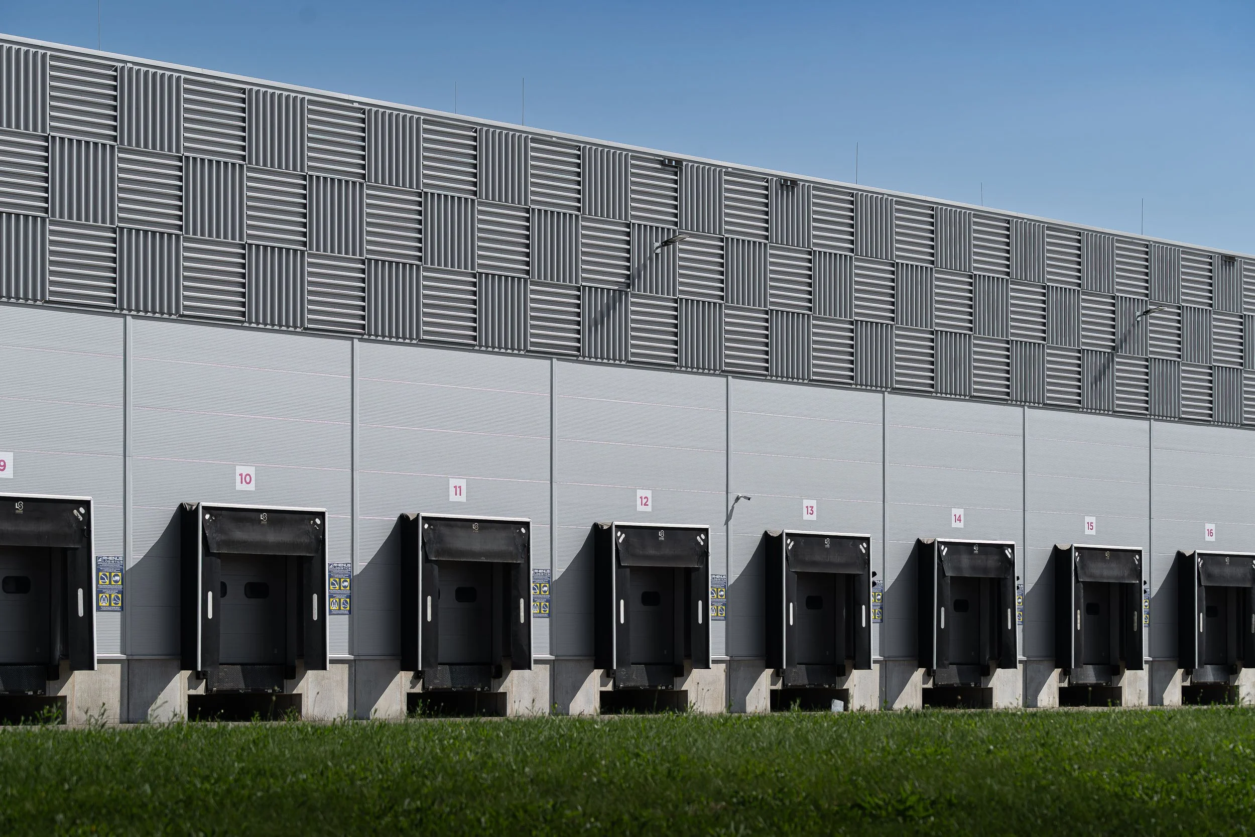 Loading dock area with black dock bumpers in front of warehouse with a metallic exterior and ventilation panels on the upper part.