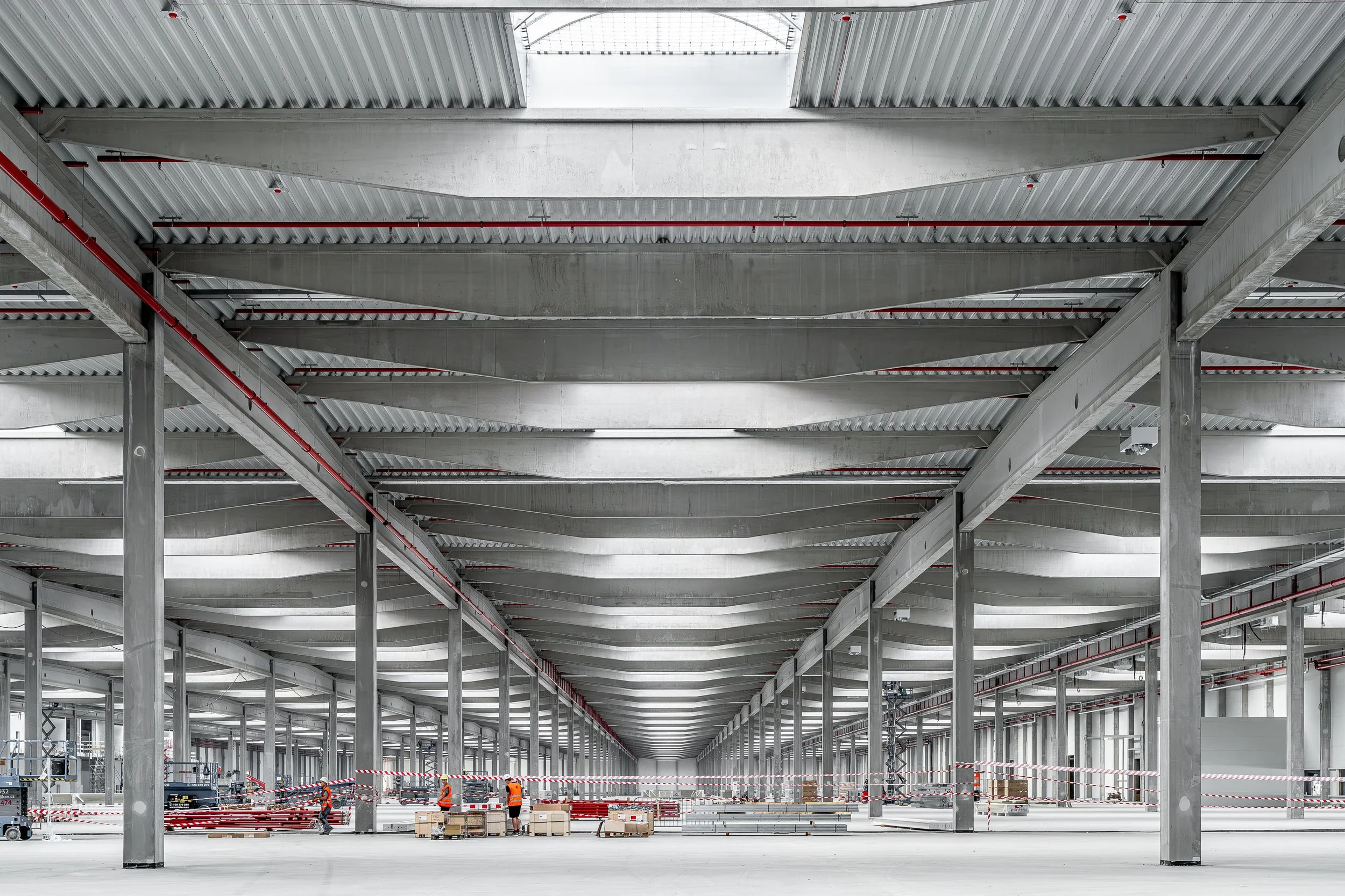 Interior view of a large warehouse or industrial facility under construction with steel beams, workers, and construction equipment.