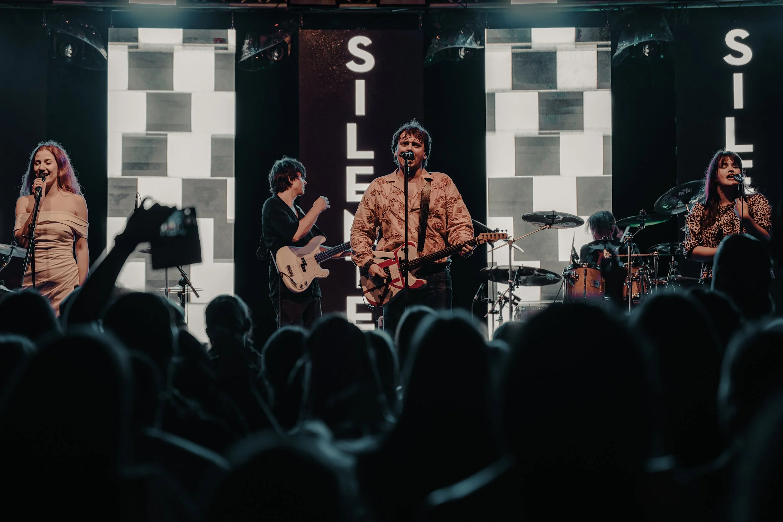 Cinematic concert photo of Croatian band performing live on stage in warm teal and orange tones.