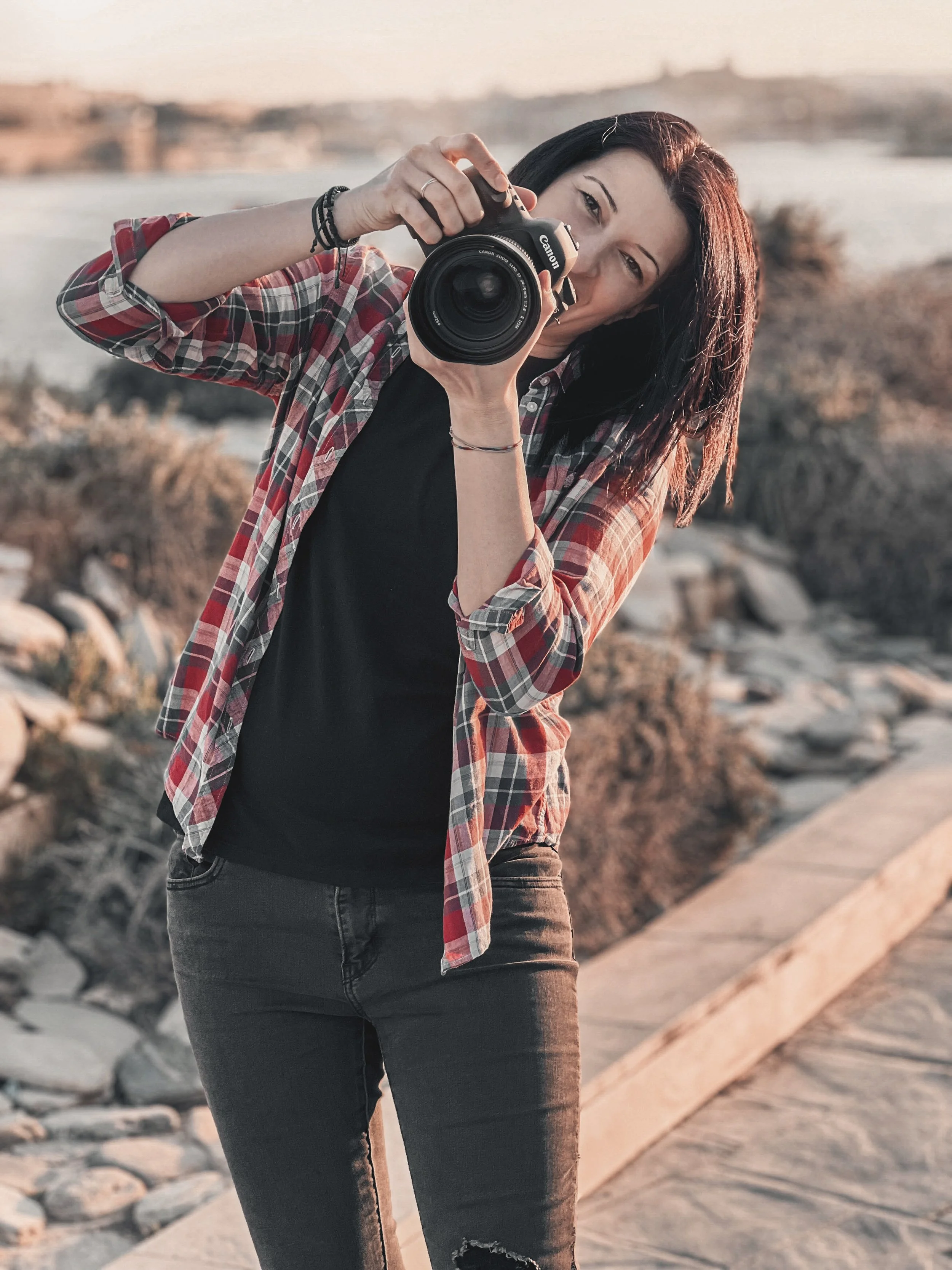 Warm cinematic portrait of female photographer with camera at sunset by the sea.
