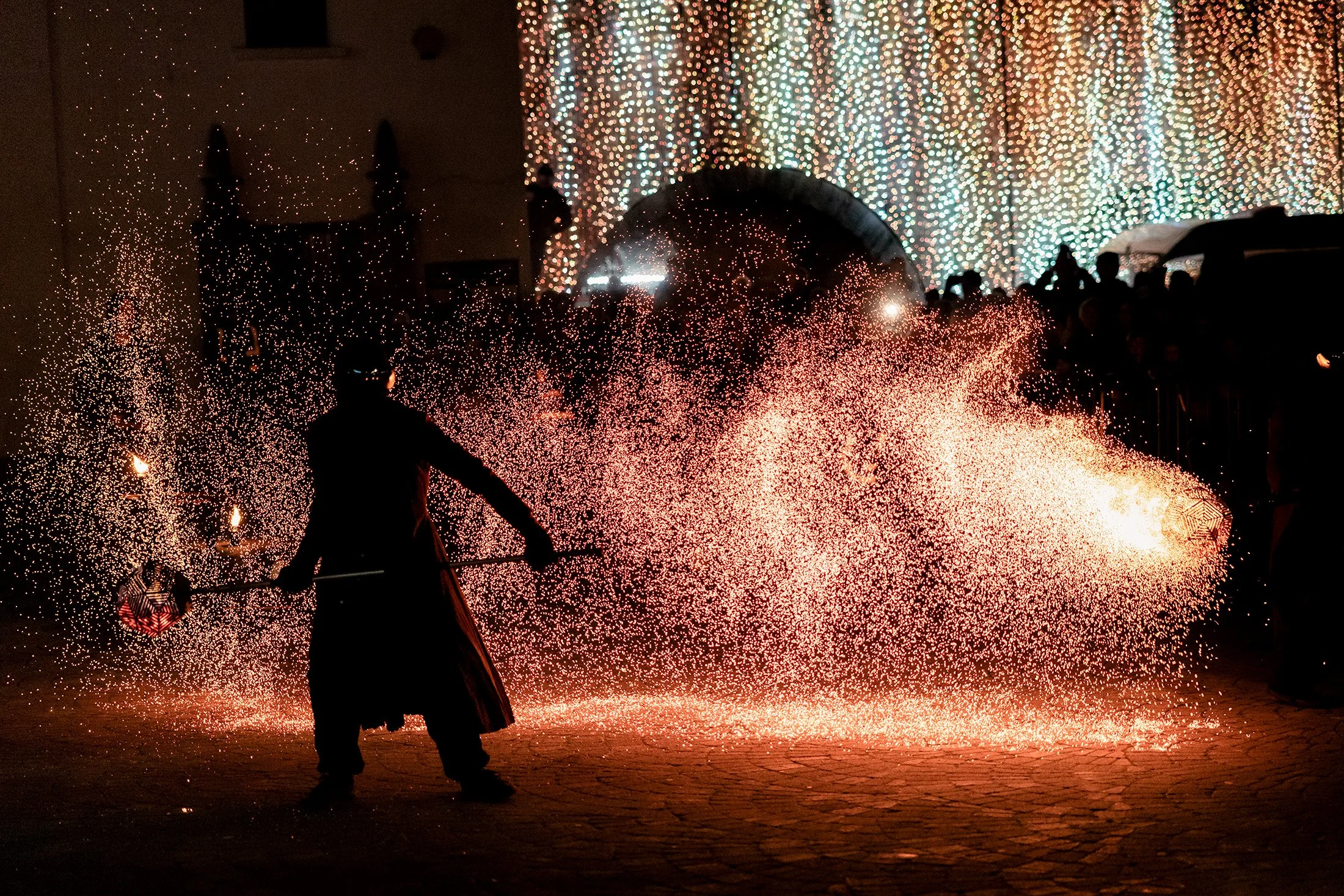 Dramatic night photo of fire performer creating sparks at an outdoor event.