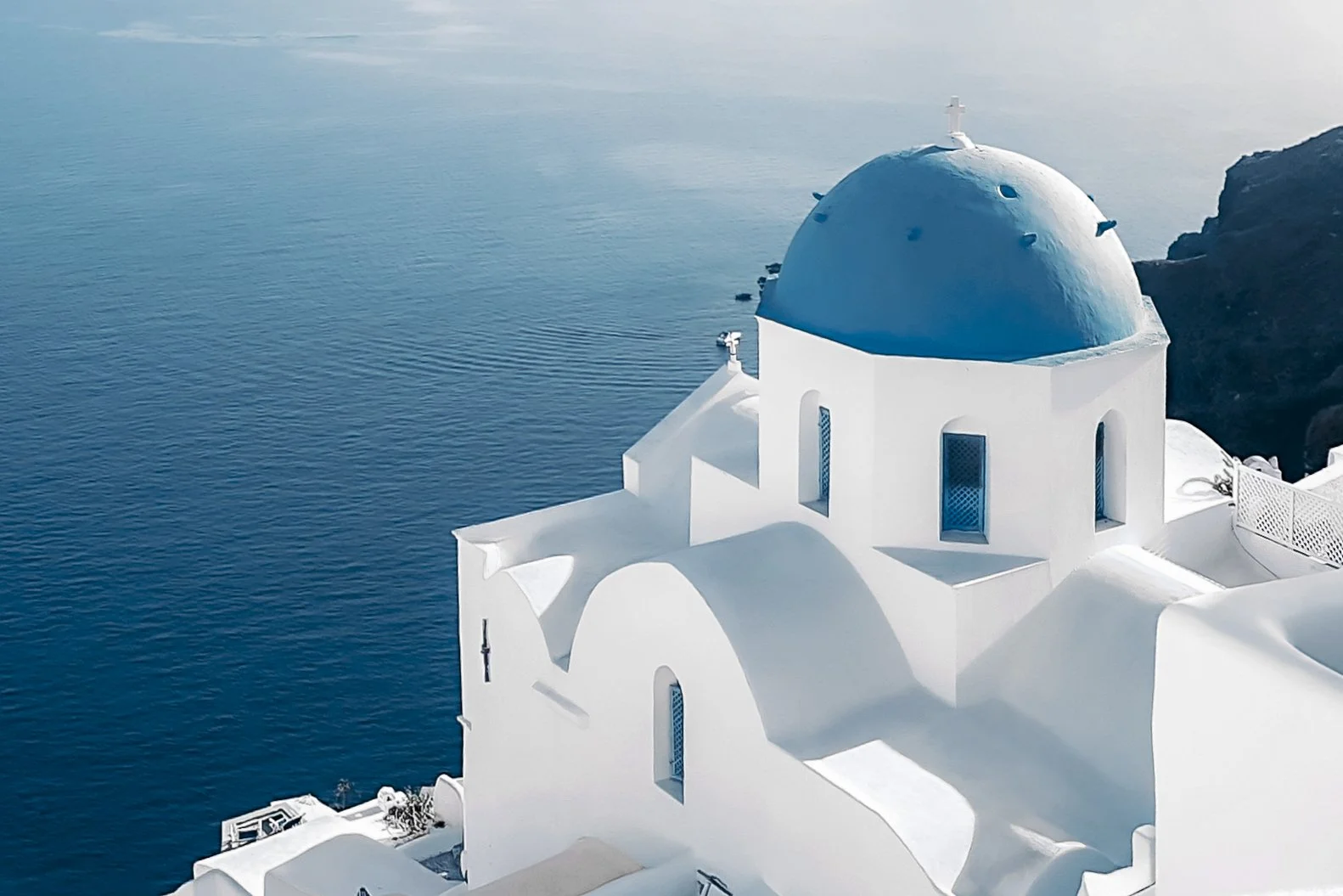 Cinematic travel photo of Santorini blue dome church above the Aegean Sea in soft pastel tones.