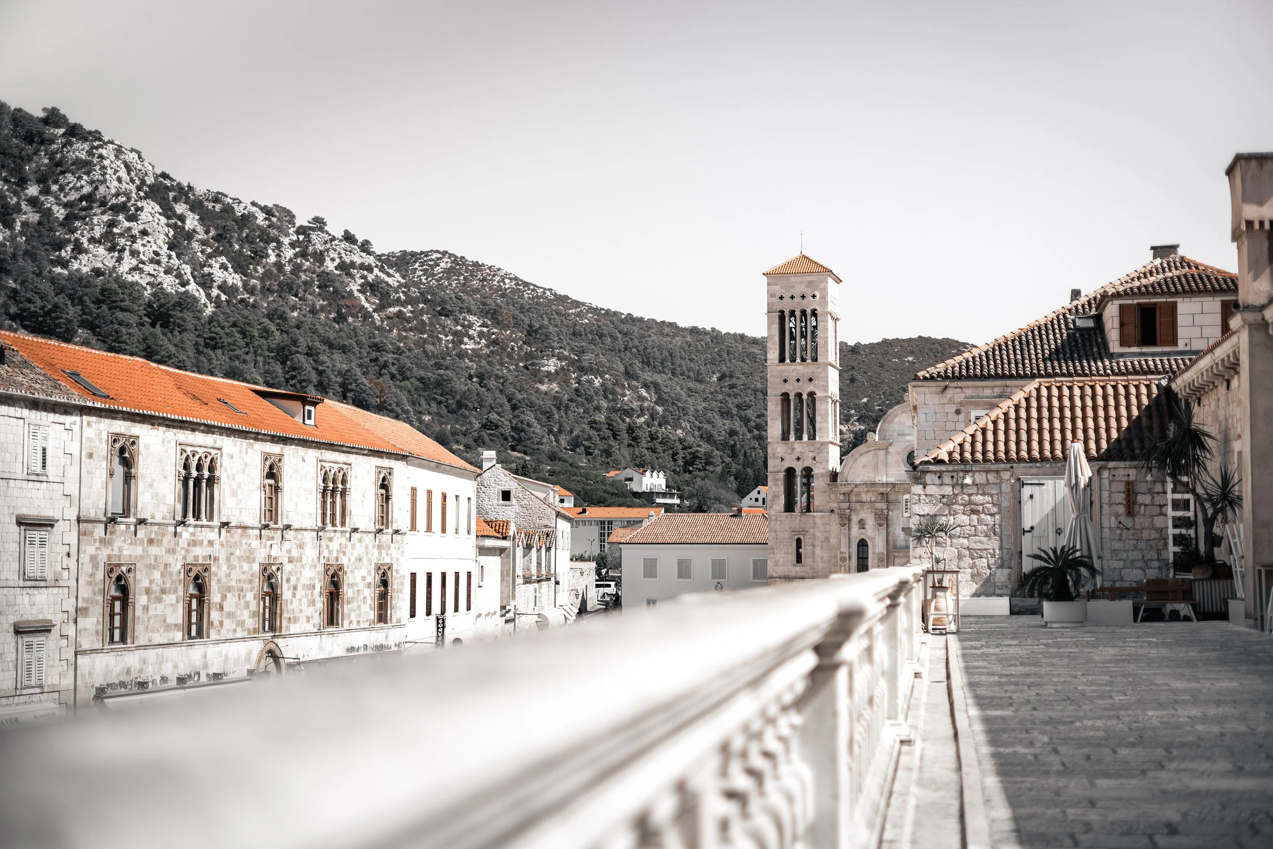 Historic stone architecture, terracotta rooftops and a church bell tower in Hvar, Croatia, with rocky Mediterranean hills in the background.