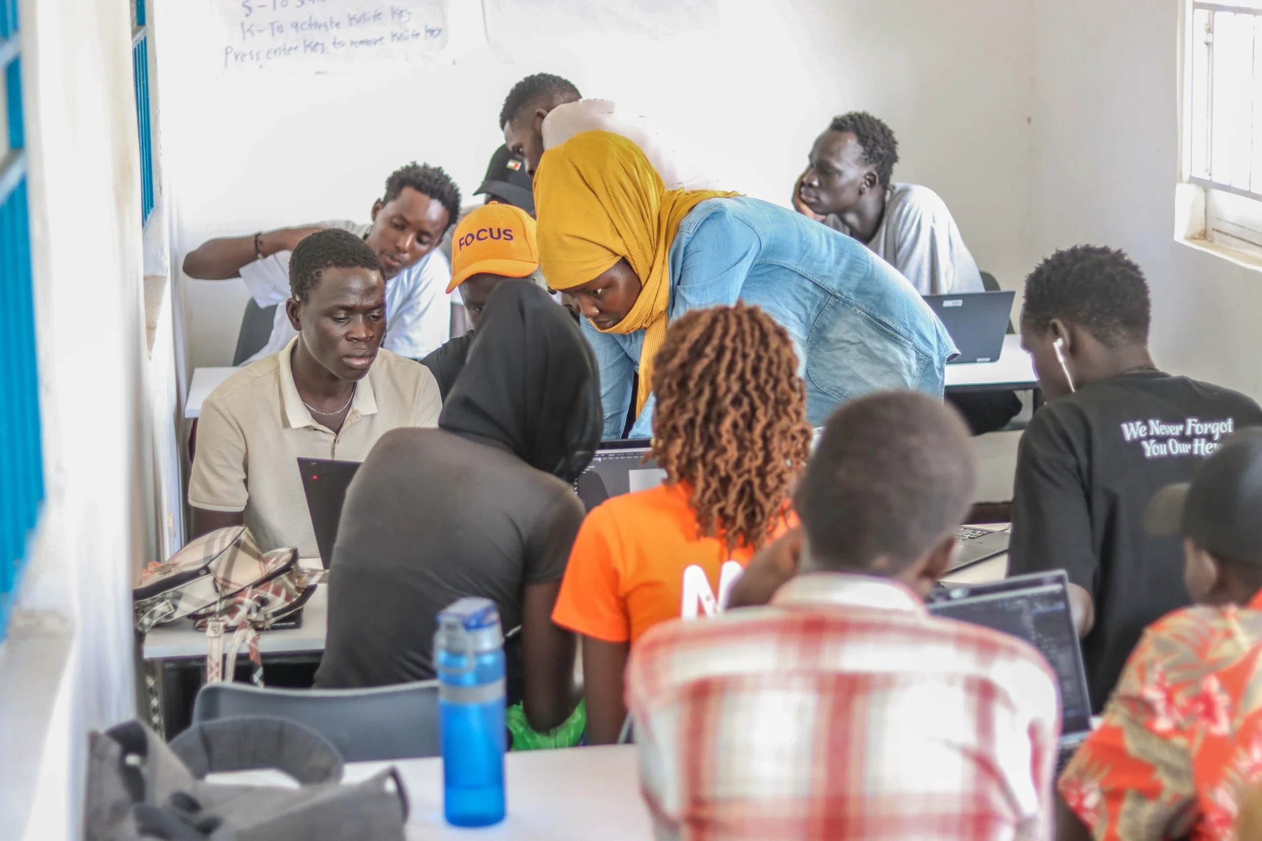 Creative Gateway participants working together around a laptop during a hands-on 3D modelling session in Kakuma Refugee Camp, Kenya.