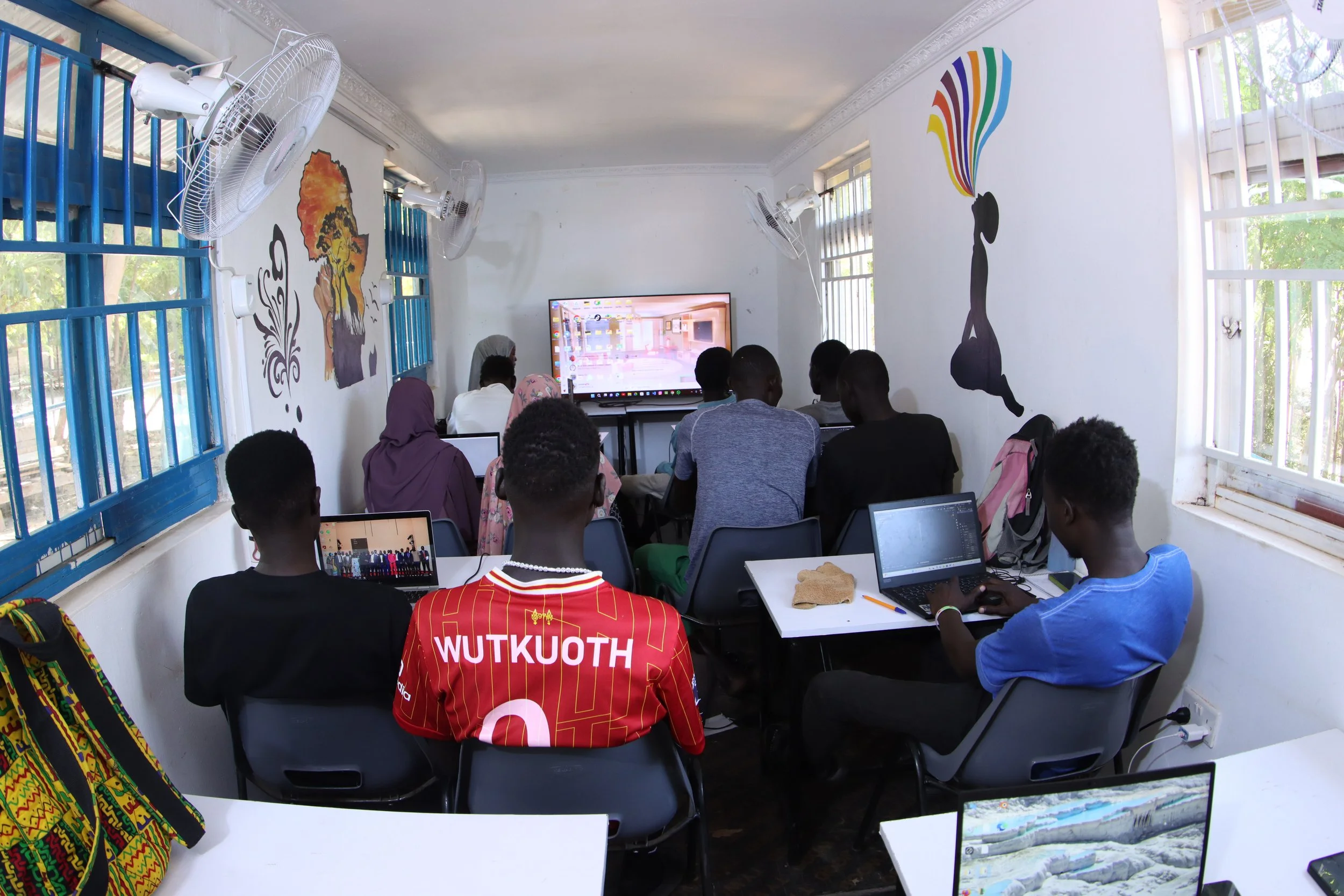 Group of students in Kakuma Refugee Camp learning 3D modelling in a digital skills training classroom at the Creative Gateway container hub, using laptops during a hands-on session for freelance and remote work opportunities