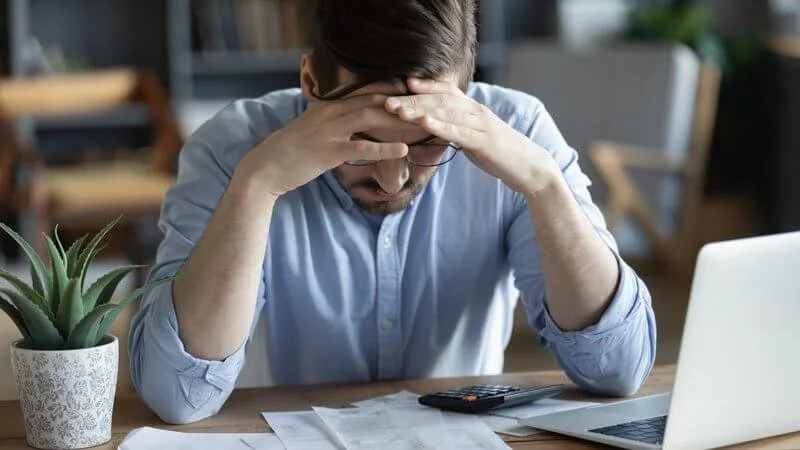 professional businessman holds head in frustration as he calculates the hidden fees in his bills