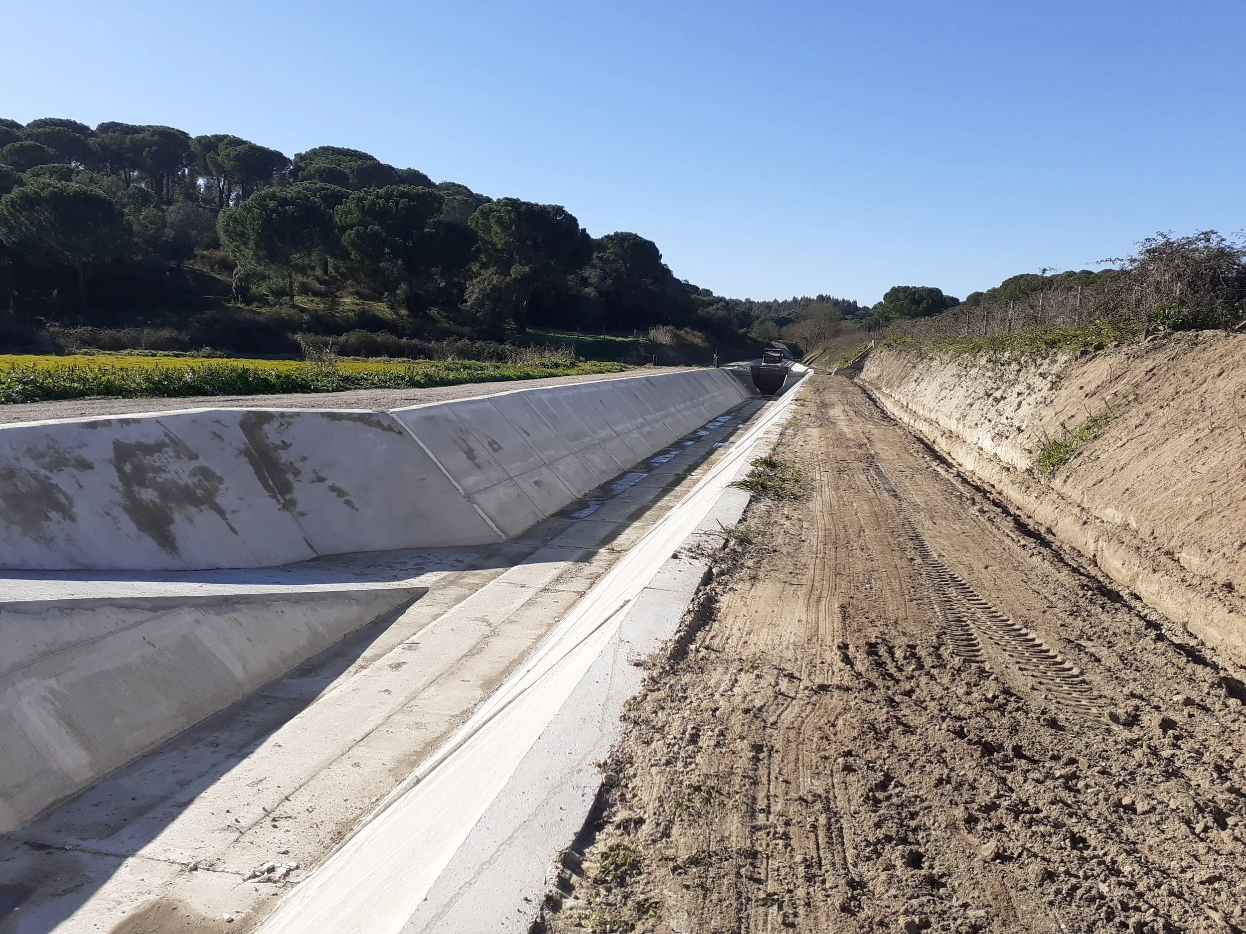 Construção de uma ponte com estrutura de concreto em uma área rural, trabalhadores no local e equipamento de construção