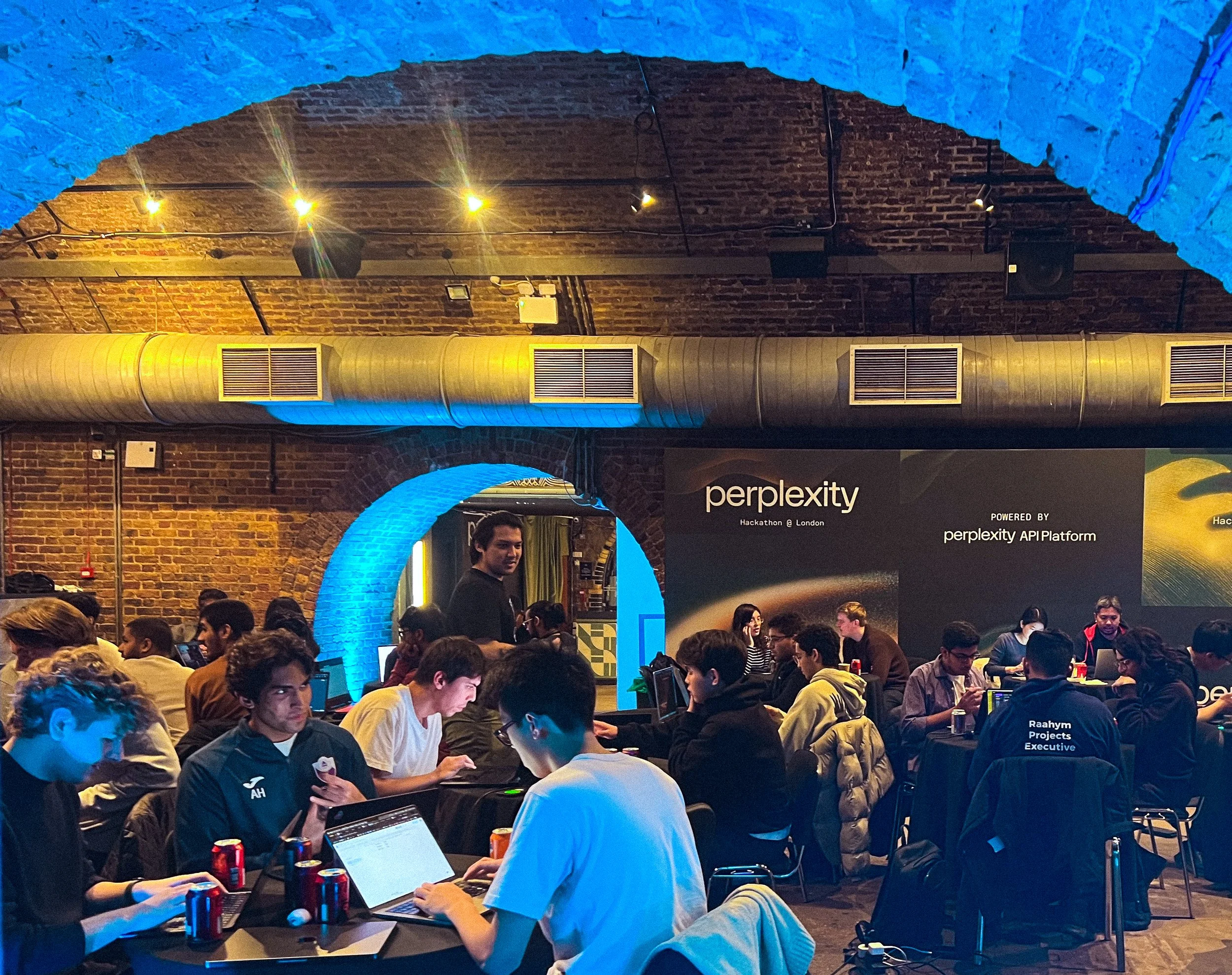 Perplexity tech event with attendees at laptops under a brick arch