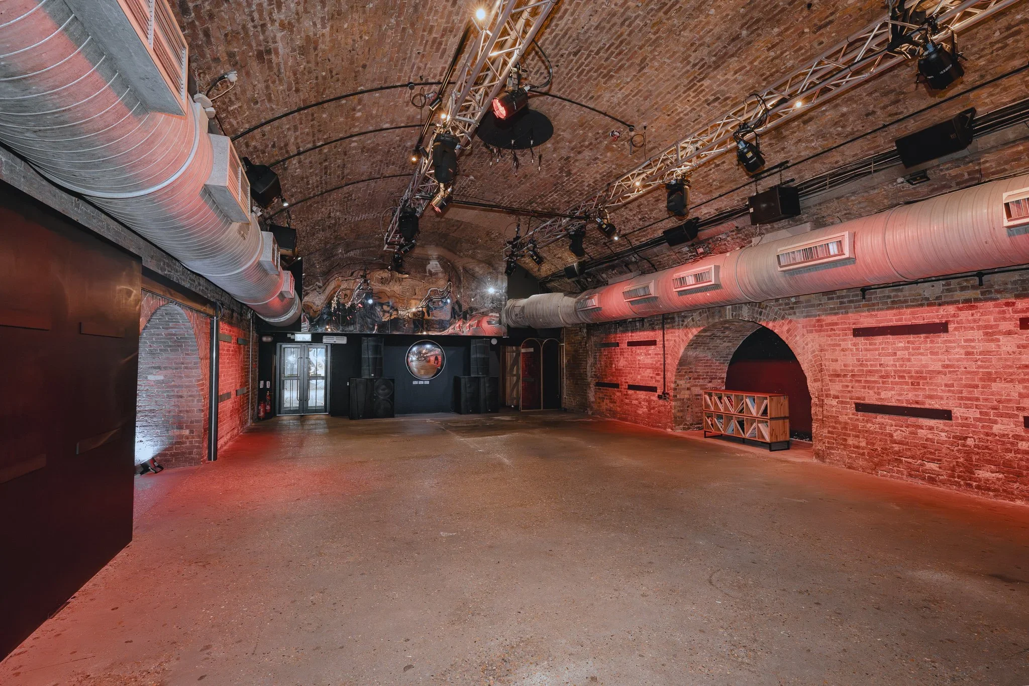 Railway arch event space with overhead lighting rig and red uplighting