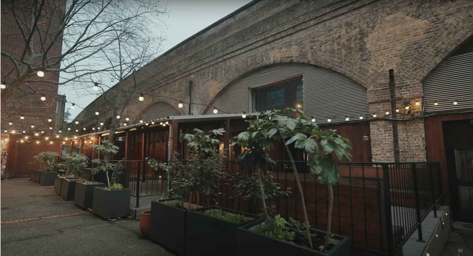 Garden terrace with planters and festoon lights beside the railway arches