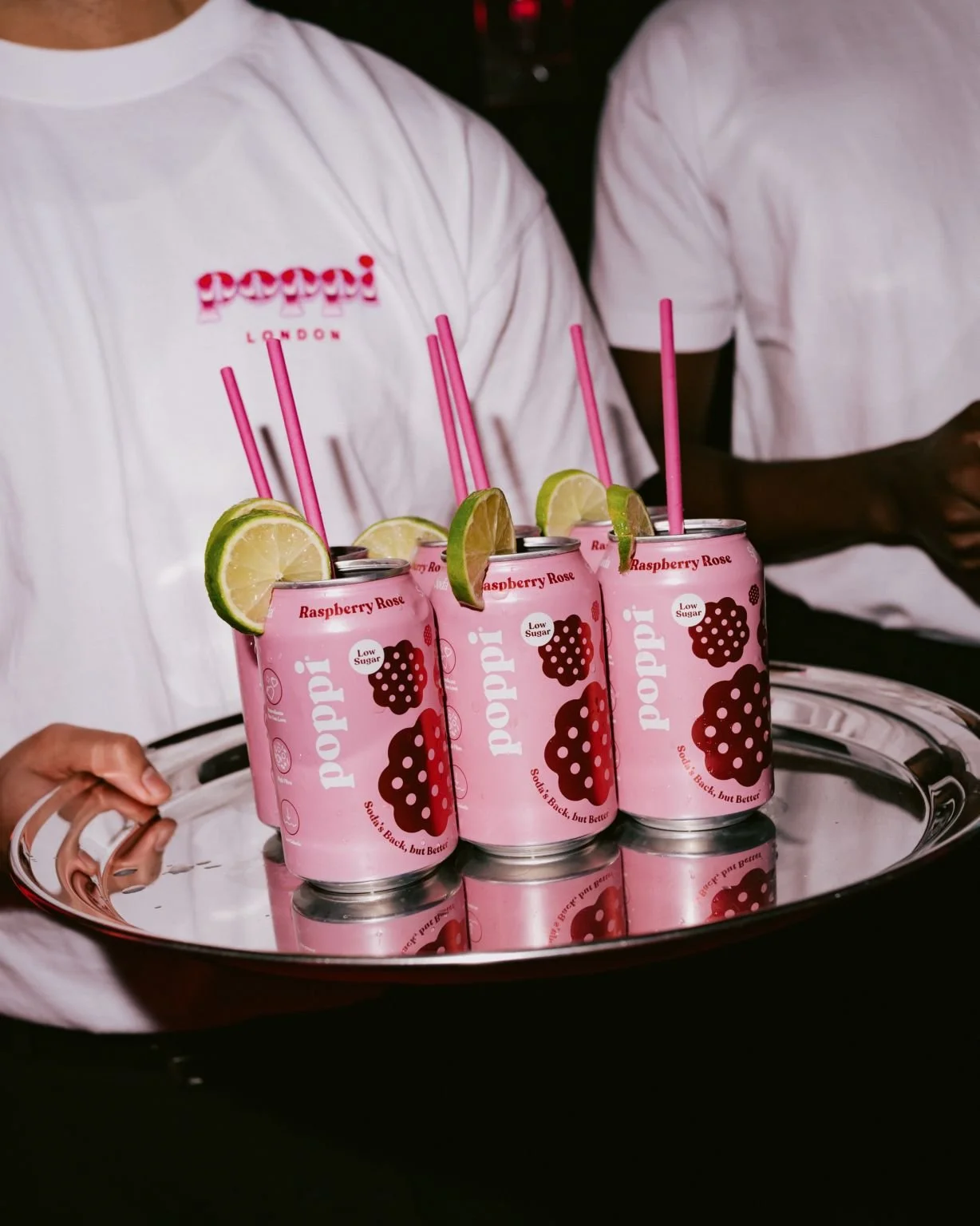 staff with white T Shirt Poppi logo carrying a tray with pink cans of Poppi raspberry rose drink, wiht lime and pink straws Poppi Brand Activation in London