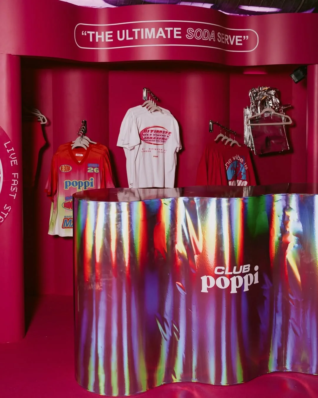 'the ultimate soda serve' print on top of pink wavy wall with Poppi merch behind a wavy hologram wrapped exhibition stand plinth brand activation inspiration