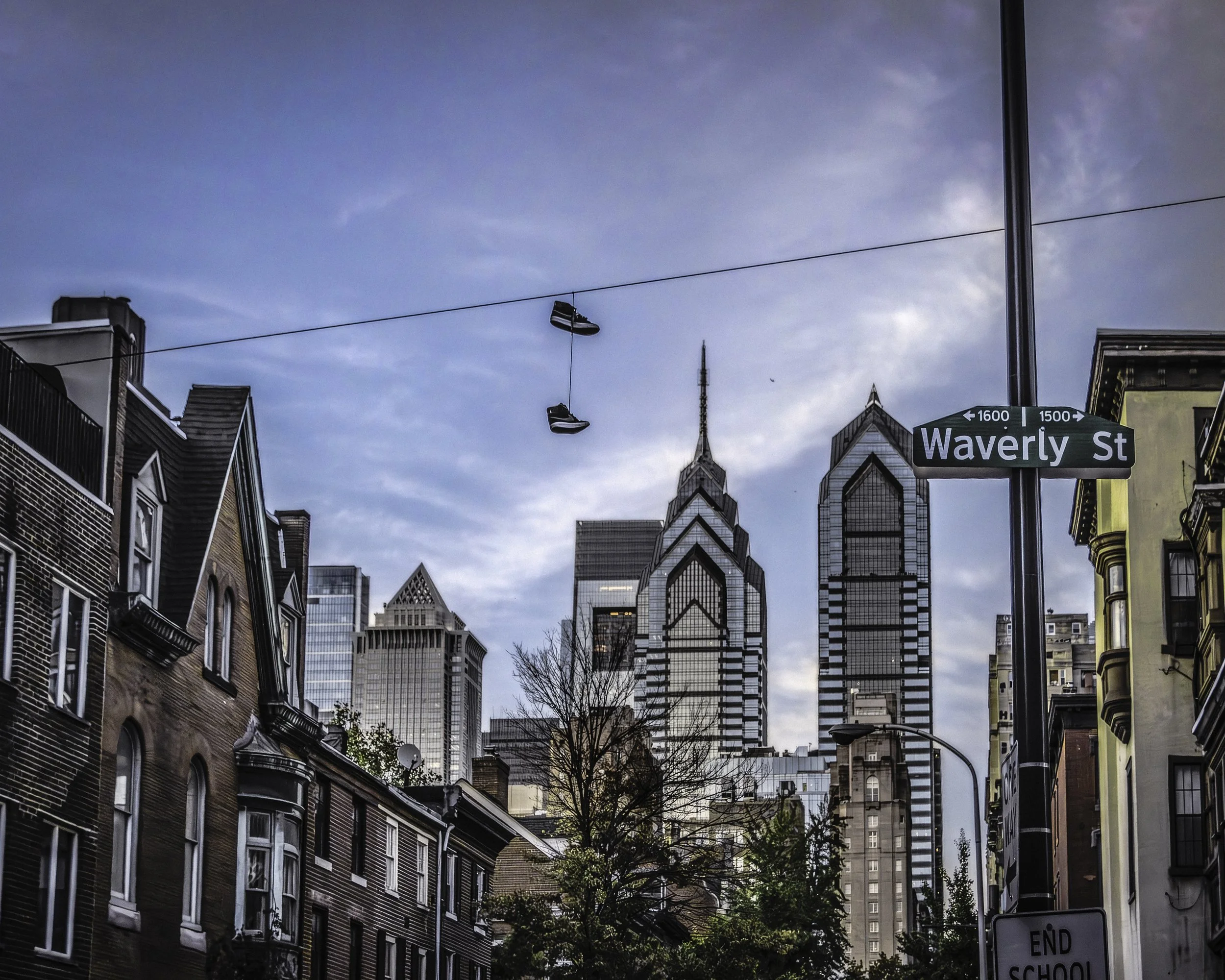 Local Wires, Global Skyline
Philadelphia skyline seen from Waverly Street, with rowhomes in the foreground, hanging sneakers on utility wires, and the Liberty Place towers rising in the distance.