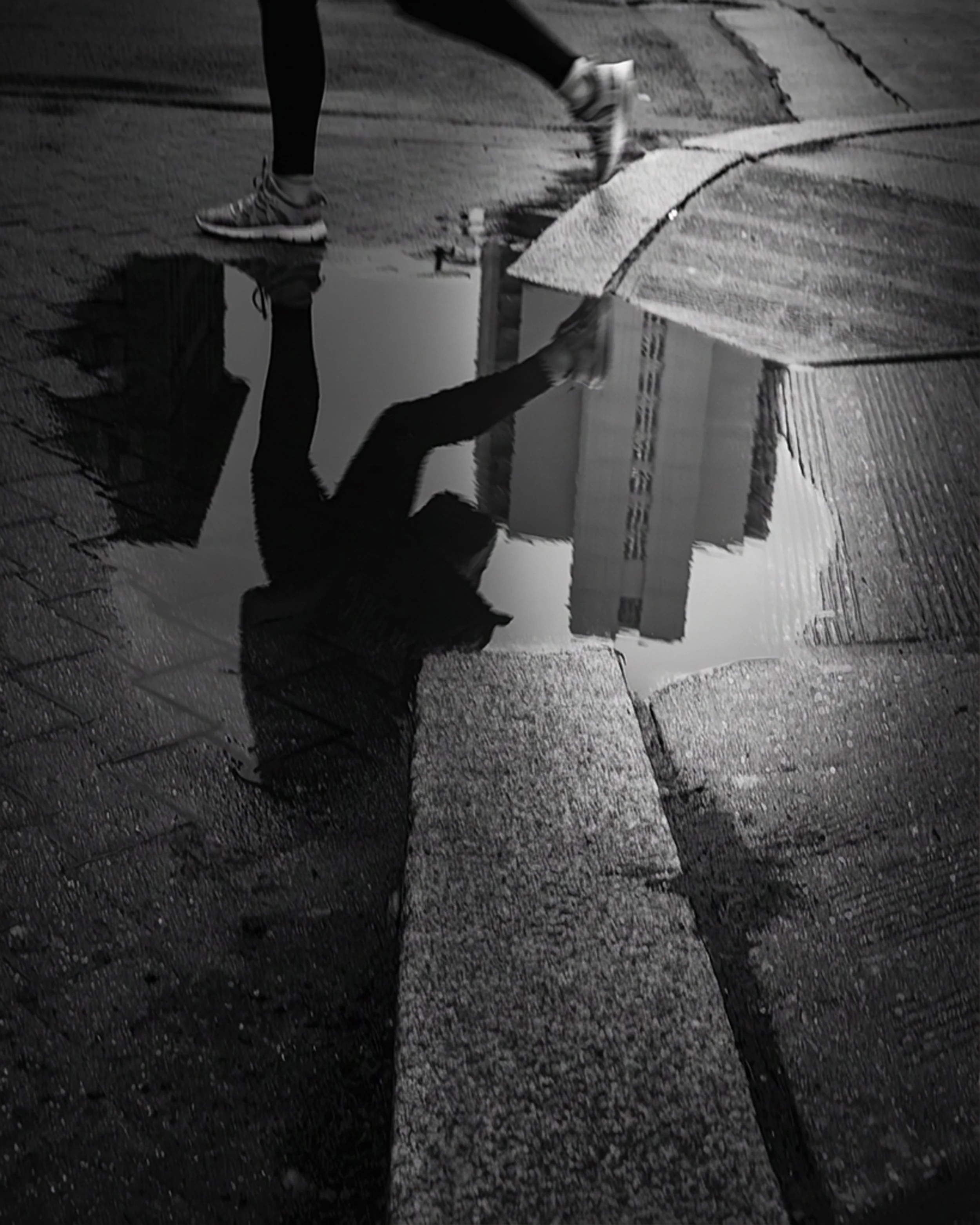 Puddle Crossing
Black and white puddle reflection of a walking figure, with legs and sneakers crossing rain-darkened pavement.