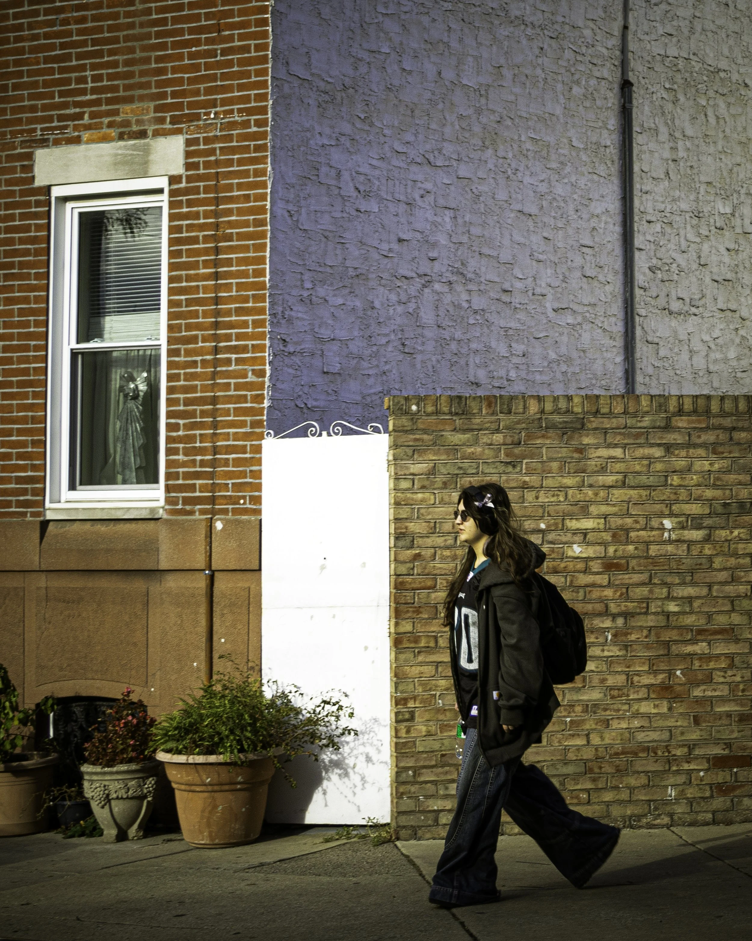 South Philly Sidewalk Rhythm
Young pedestrian walks past a brick wall and house window along a quiet neighborhood sidewalk. 