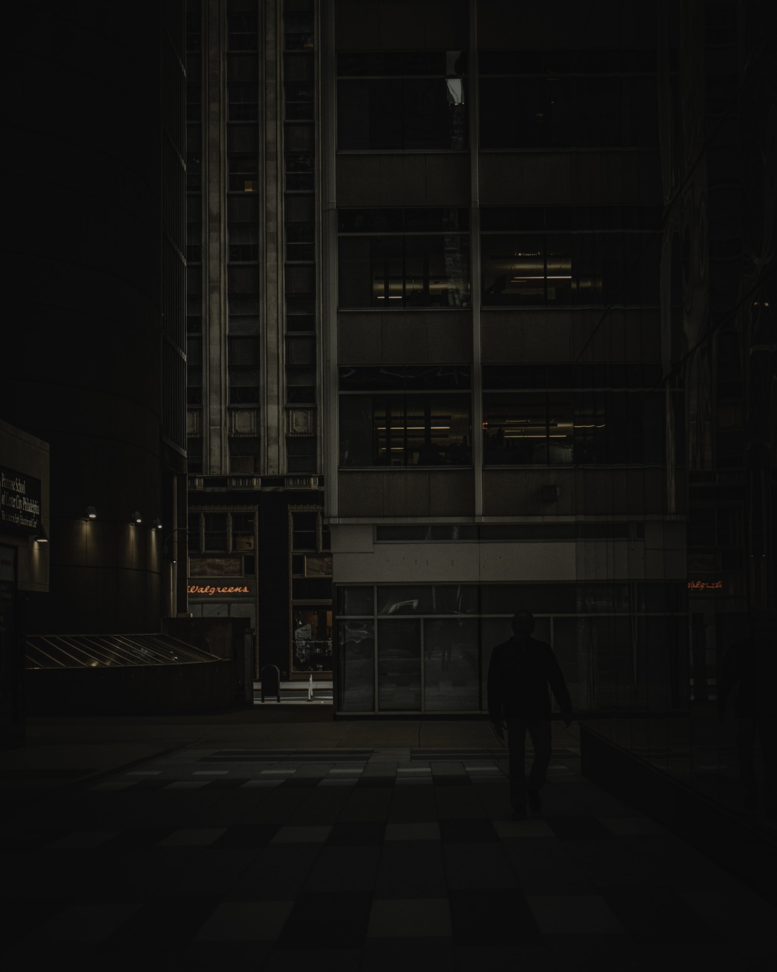 Figure in the Plaza
Solitary figure walking through a dark plaza beside a glass office building at night.