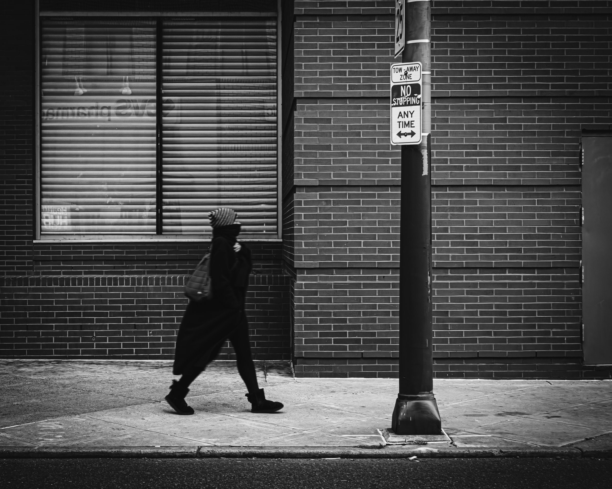 No Stopping, Still Passing
Black and white street photograph of a blurred pedestrian walking past a brick wall and a no-stopping sign on 15th Street behind the Kimmel Center for the Performing Arts.