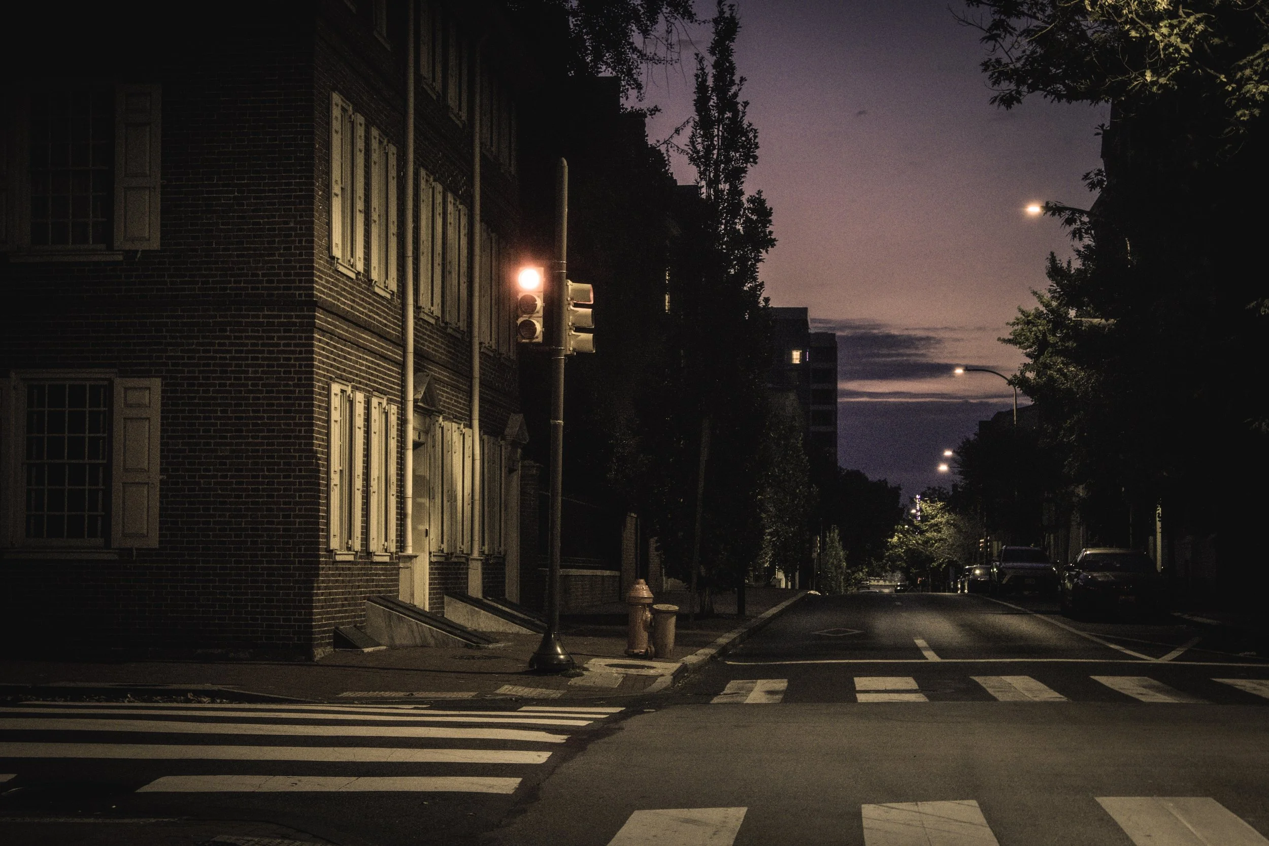 Before the City Moves
Quiet Philadelphia street corner with brick rowhouses, crosswalk lines, and a red traffic light at dawn.