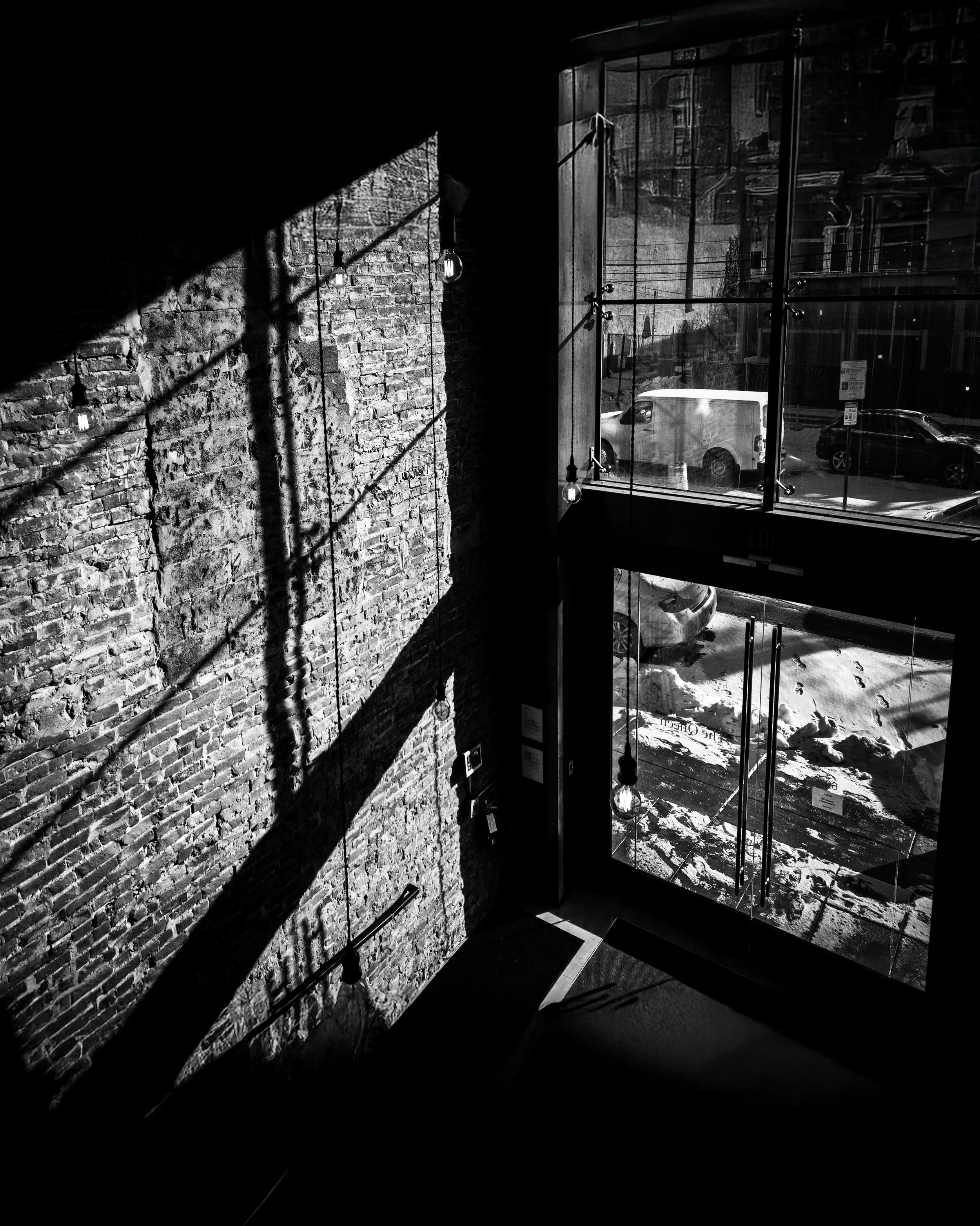 Threshold at The Queen
Black and white interior view at Sosuite at The Queen in Queen Village, showing a brick wall and glass entryway marked by strong window shadows and reflections.
