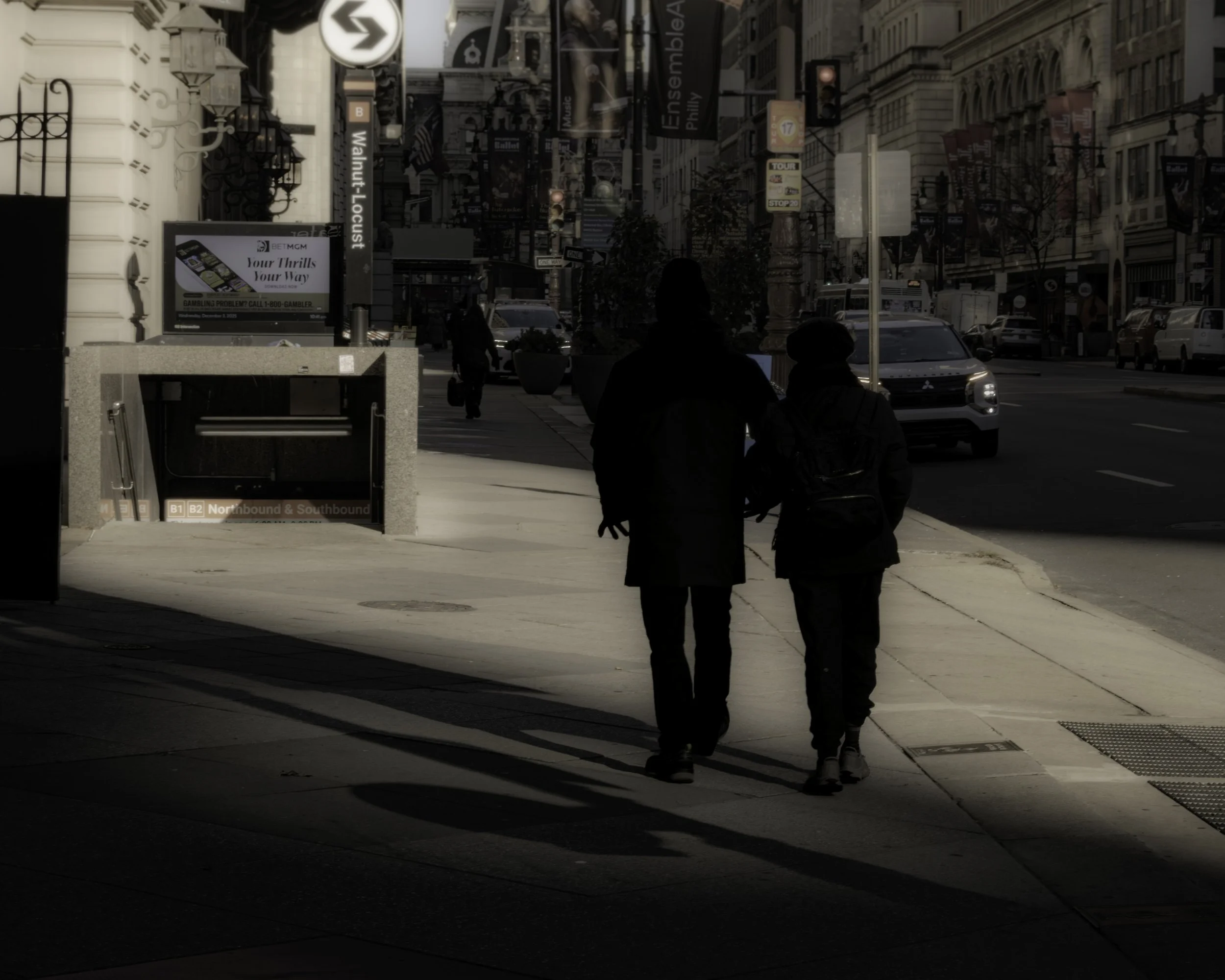 Entering the Light
Two pedestrians walk through a bright patch of sidewalk light near a Walnut-Locust station entrance in downtown Philadelphia.
