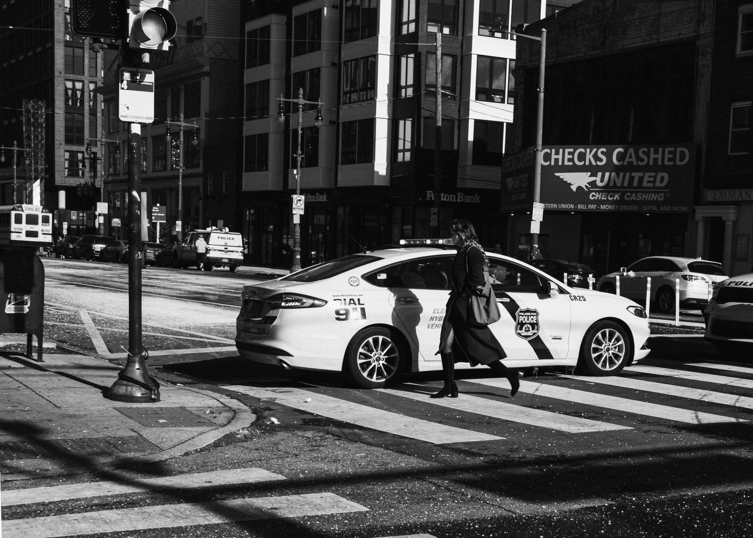 Bright Intersection
Black and white street photograph of a woman crossing in front of a parked police car at a bright intersection.